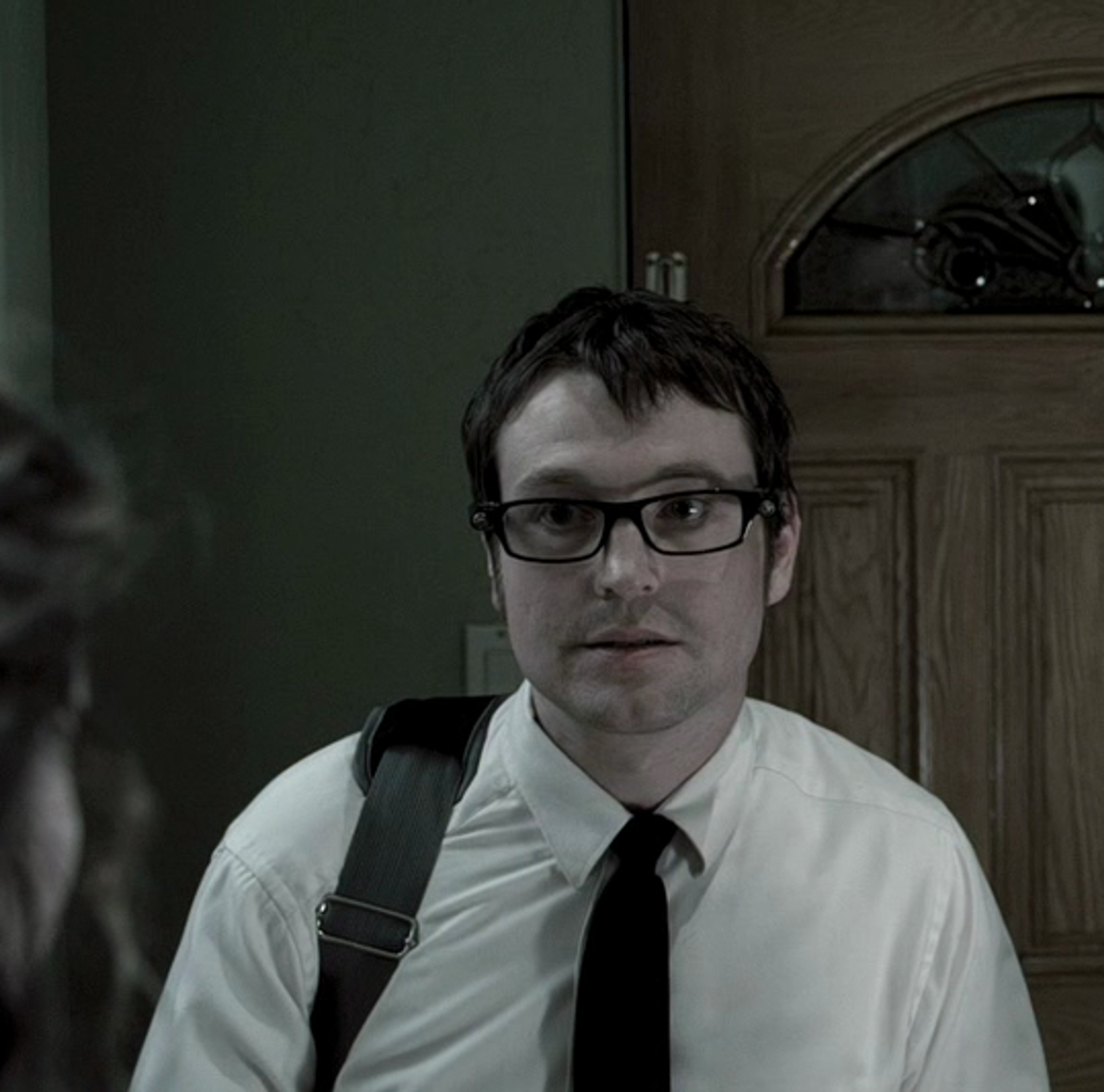 A man with glasses wearing a white shirt and black tie, with a serious expression on his face.