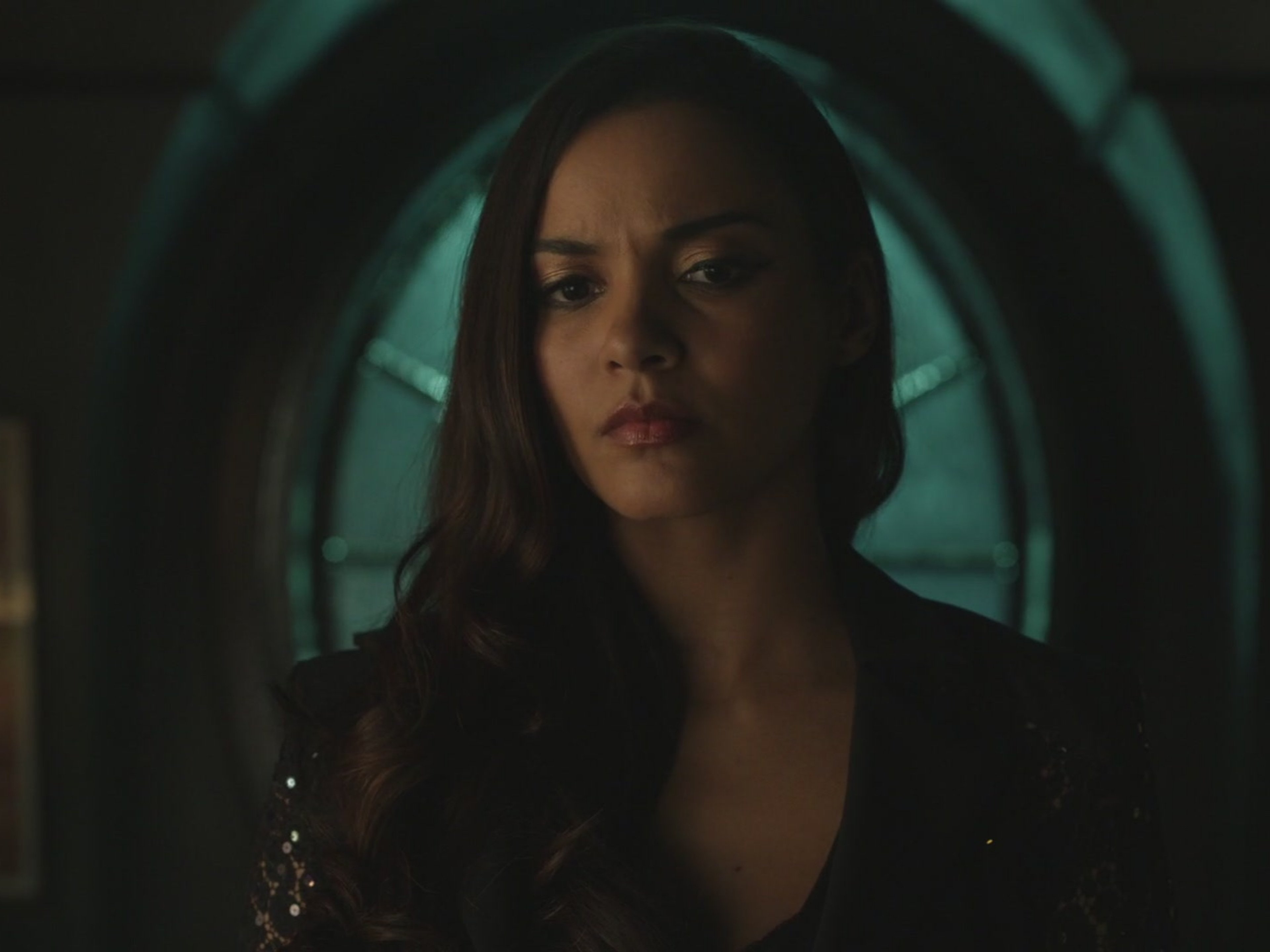 A woman with dark hair wearing a black outfit in a dimly lit, industrial setting