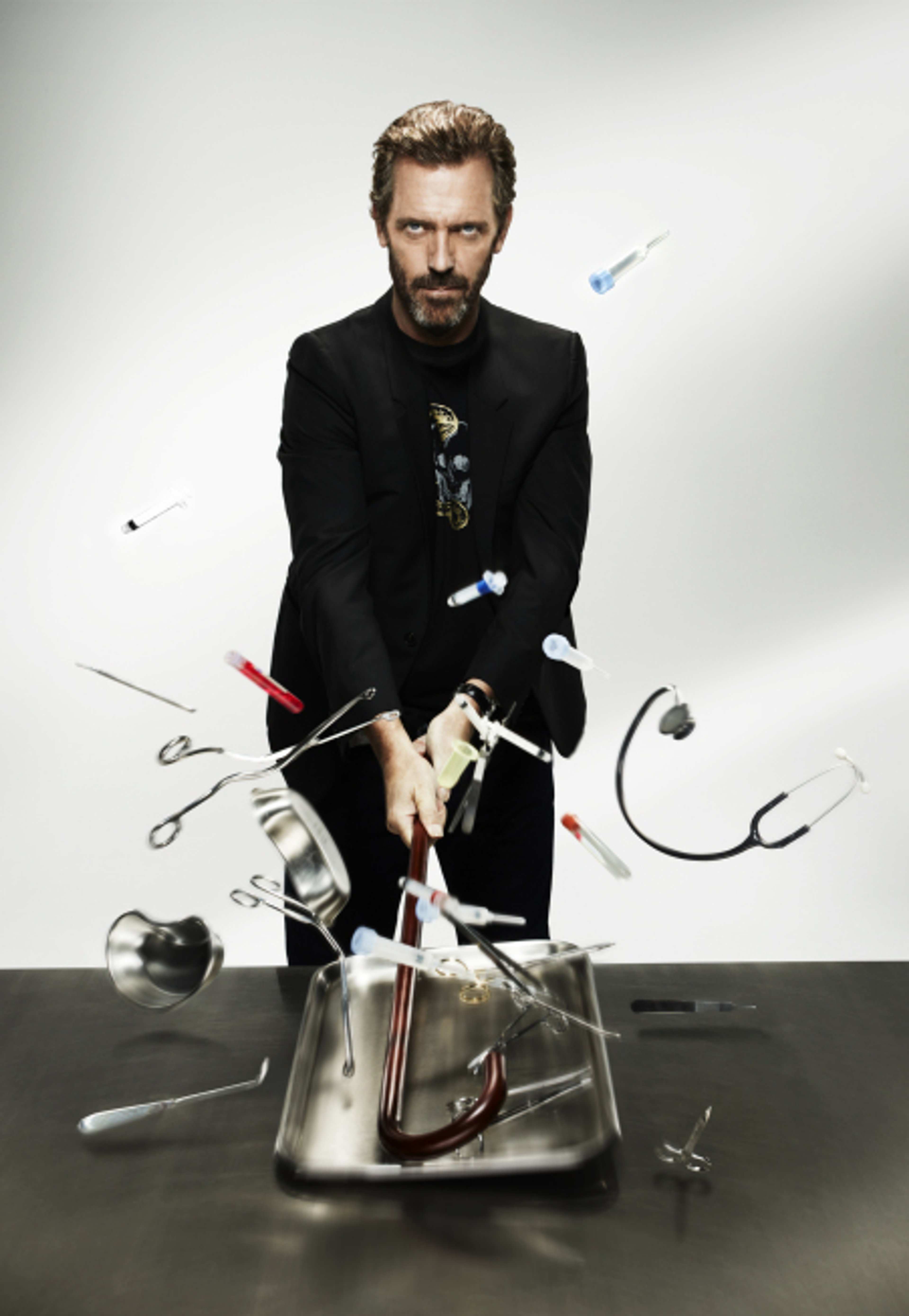 A man in a black suit sitting at a desk surrounded by medical equipment