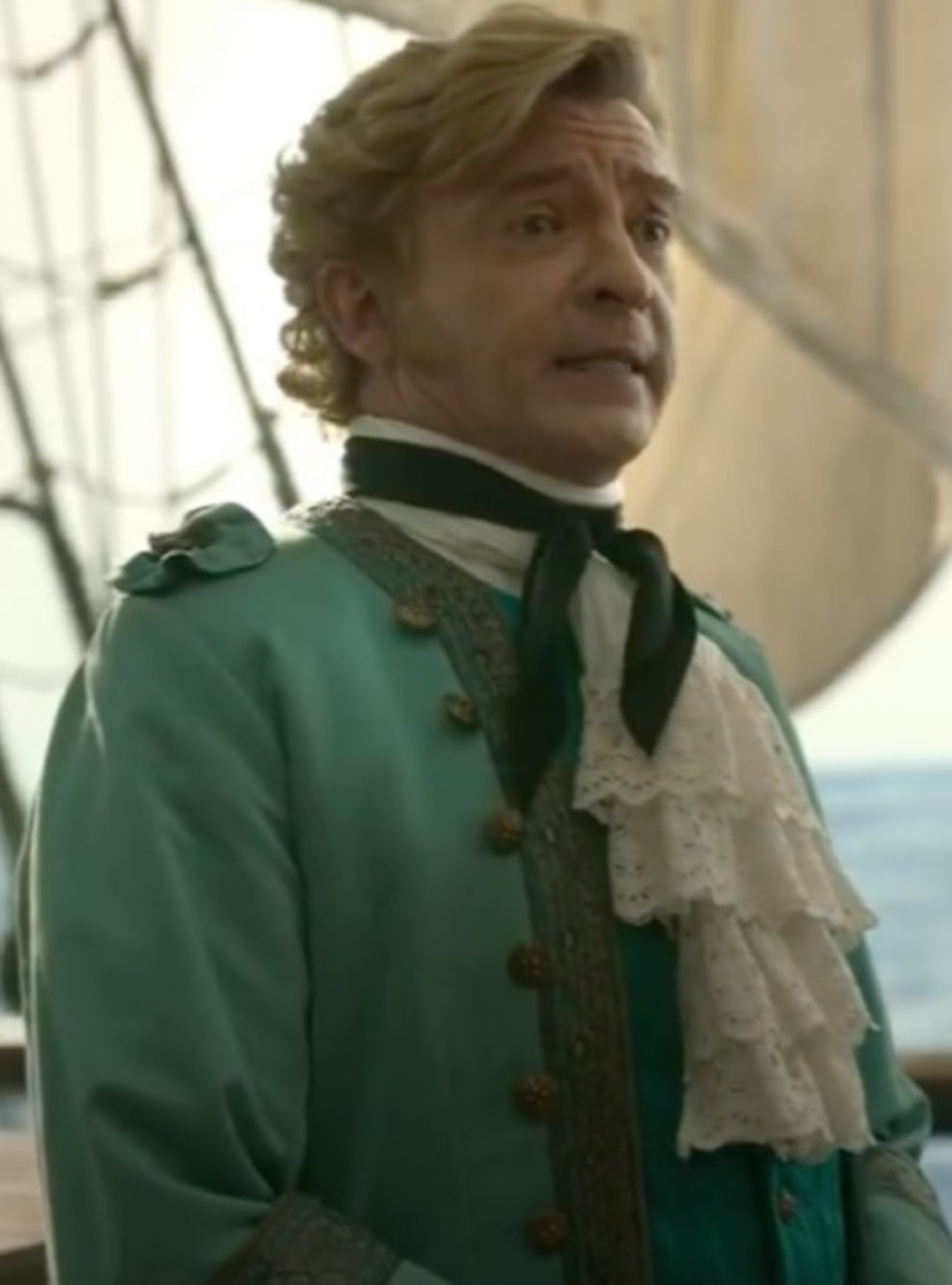 An older man in a green coat and white ruffled shirt on a ship or boat