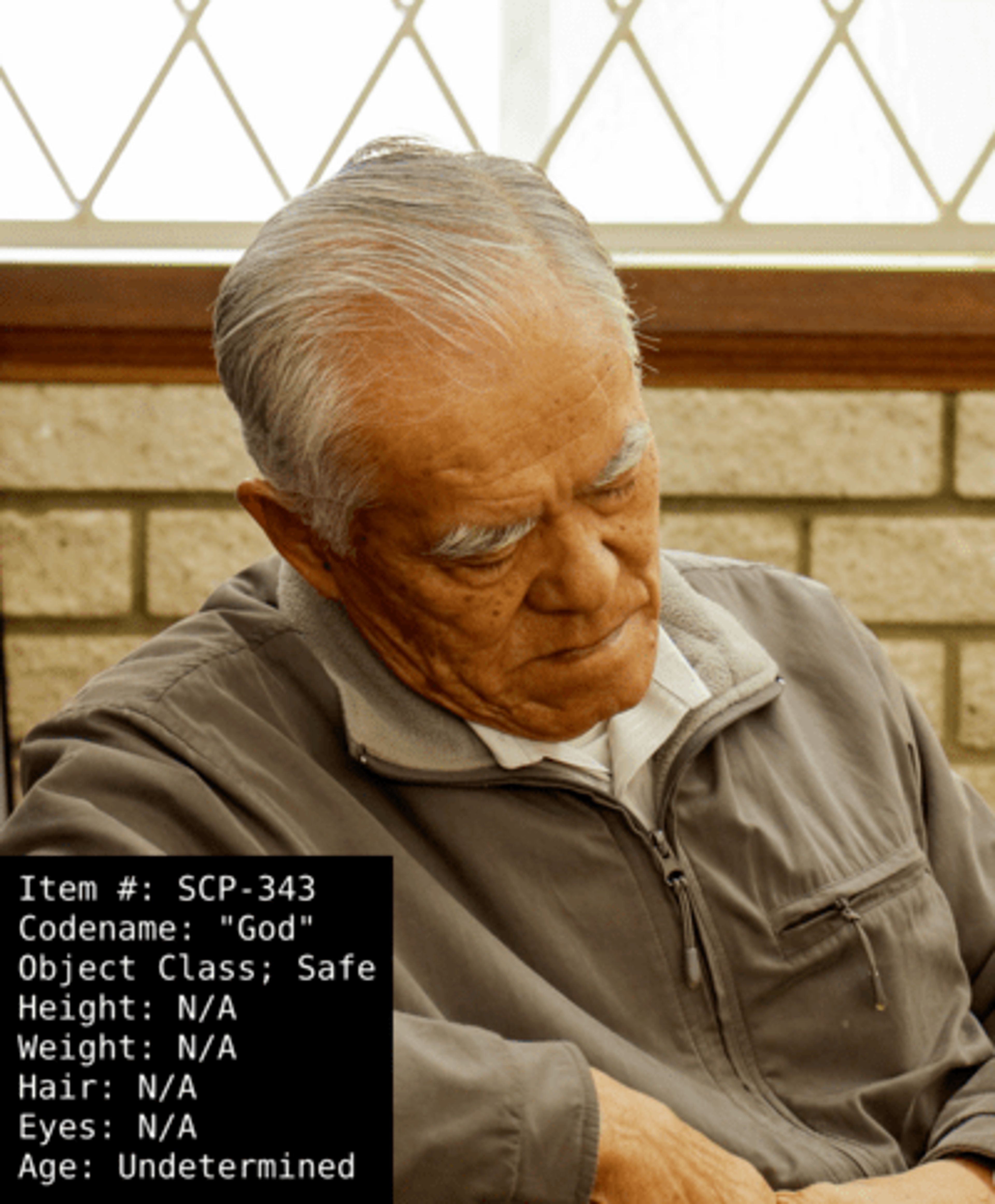 An elderly man with gray hair and a wrinkled face, wearing a gray jacket or sweater and looking down with a serious expression.