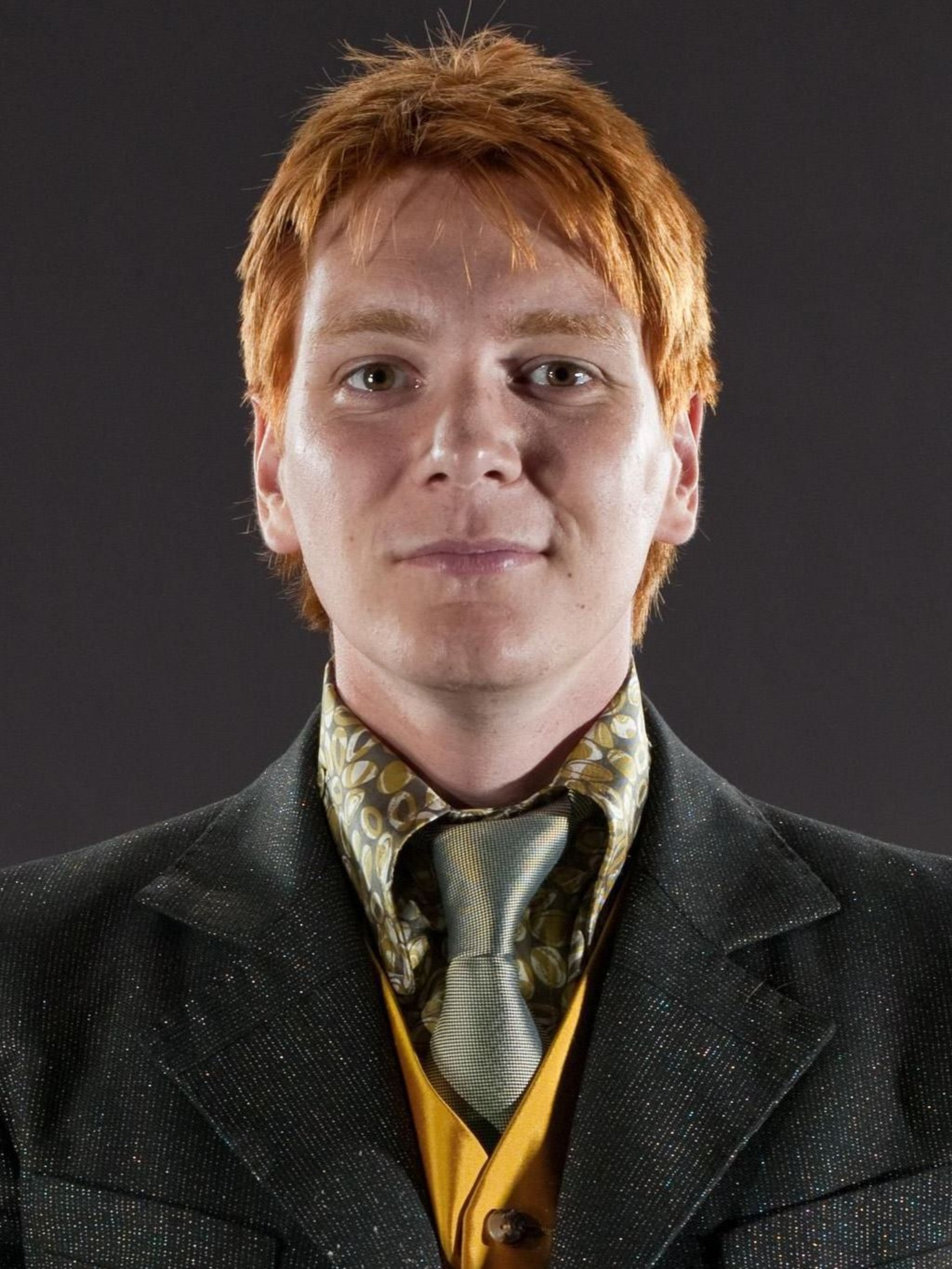 A young man with red hair and freckles wearing a black suit jacket and yellow vest