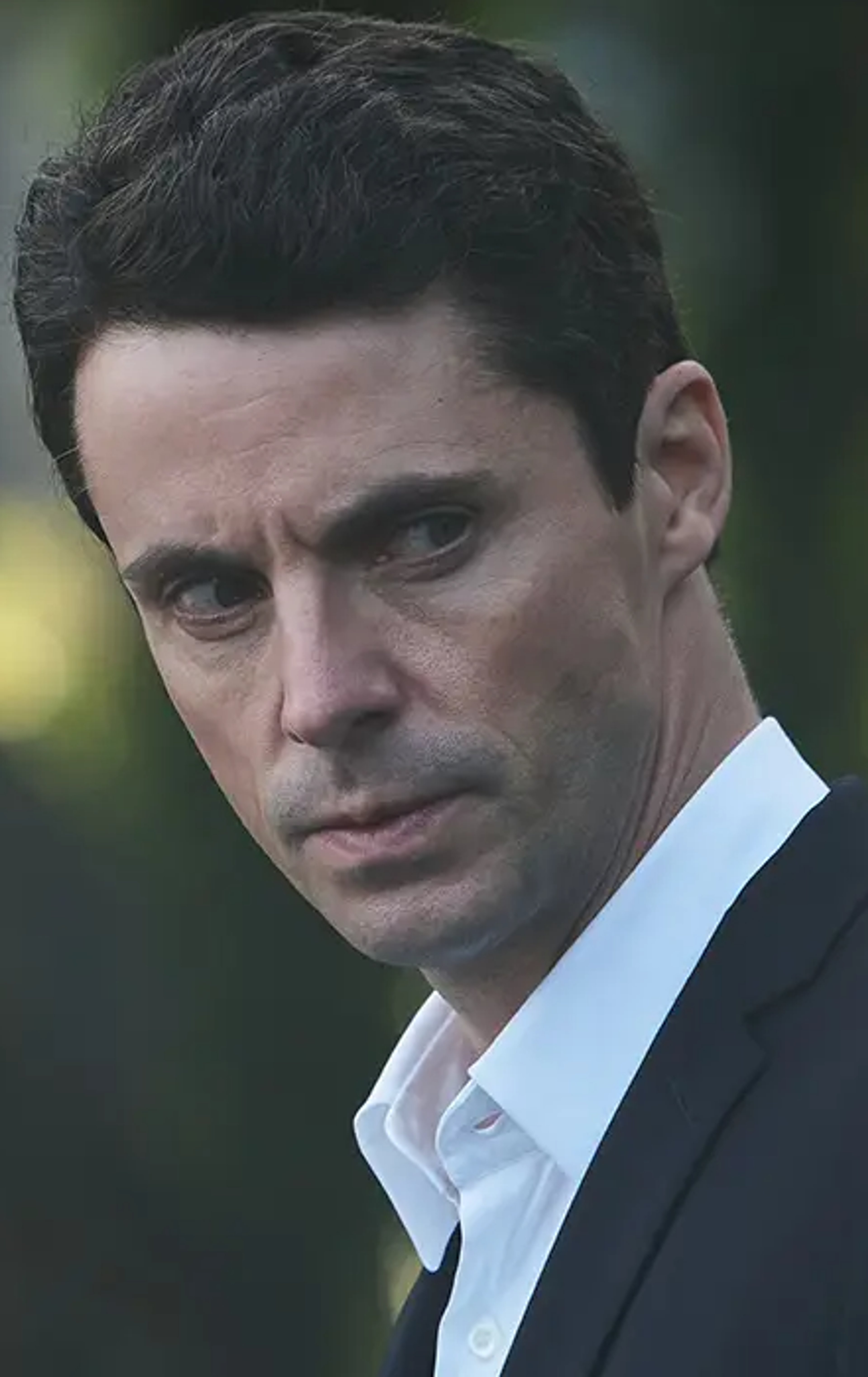 A serious-looking man with dark hair and gray eyes, wearing a suit