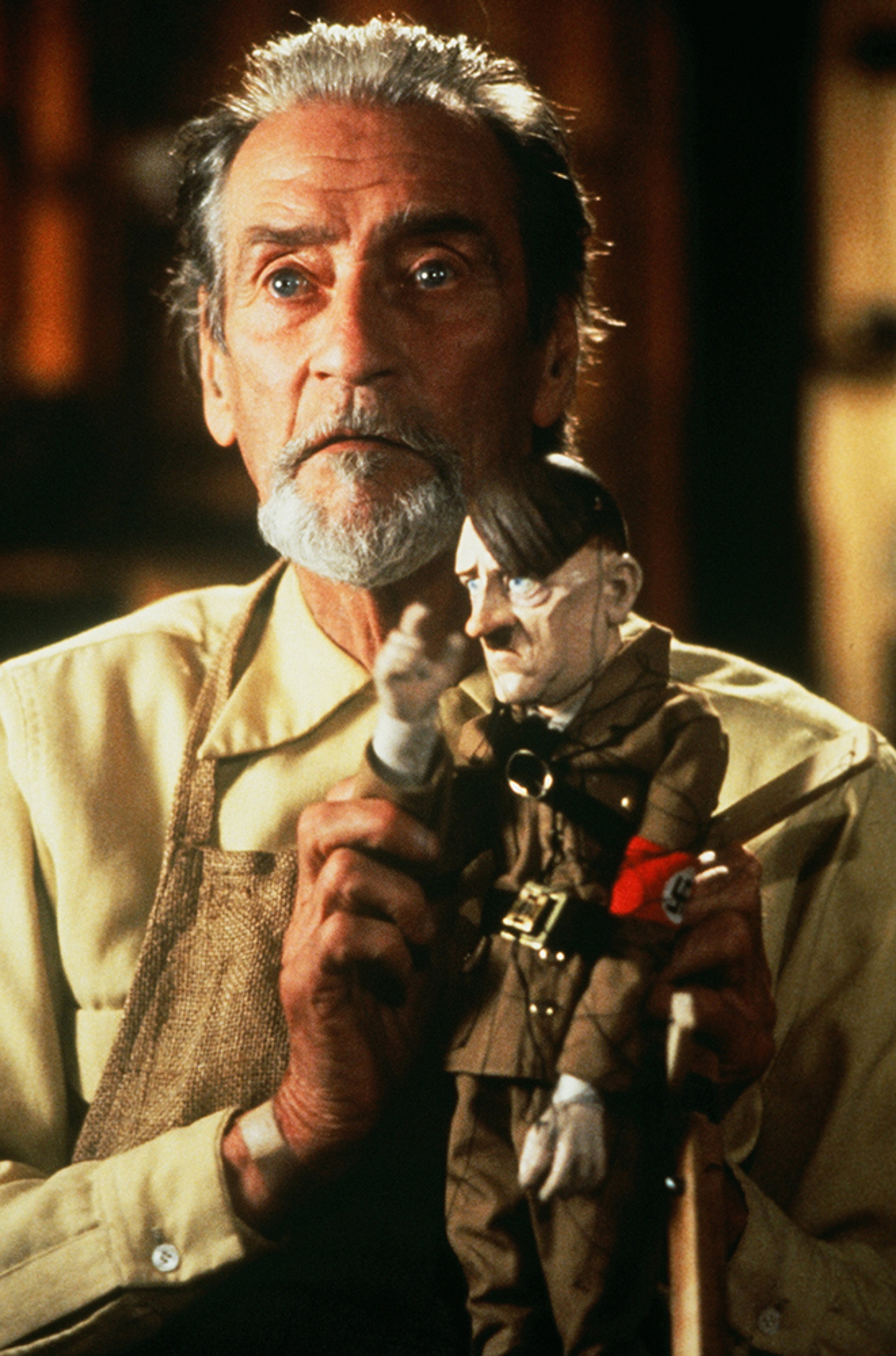 An older man with a white beard holding a wooden puppet