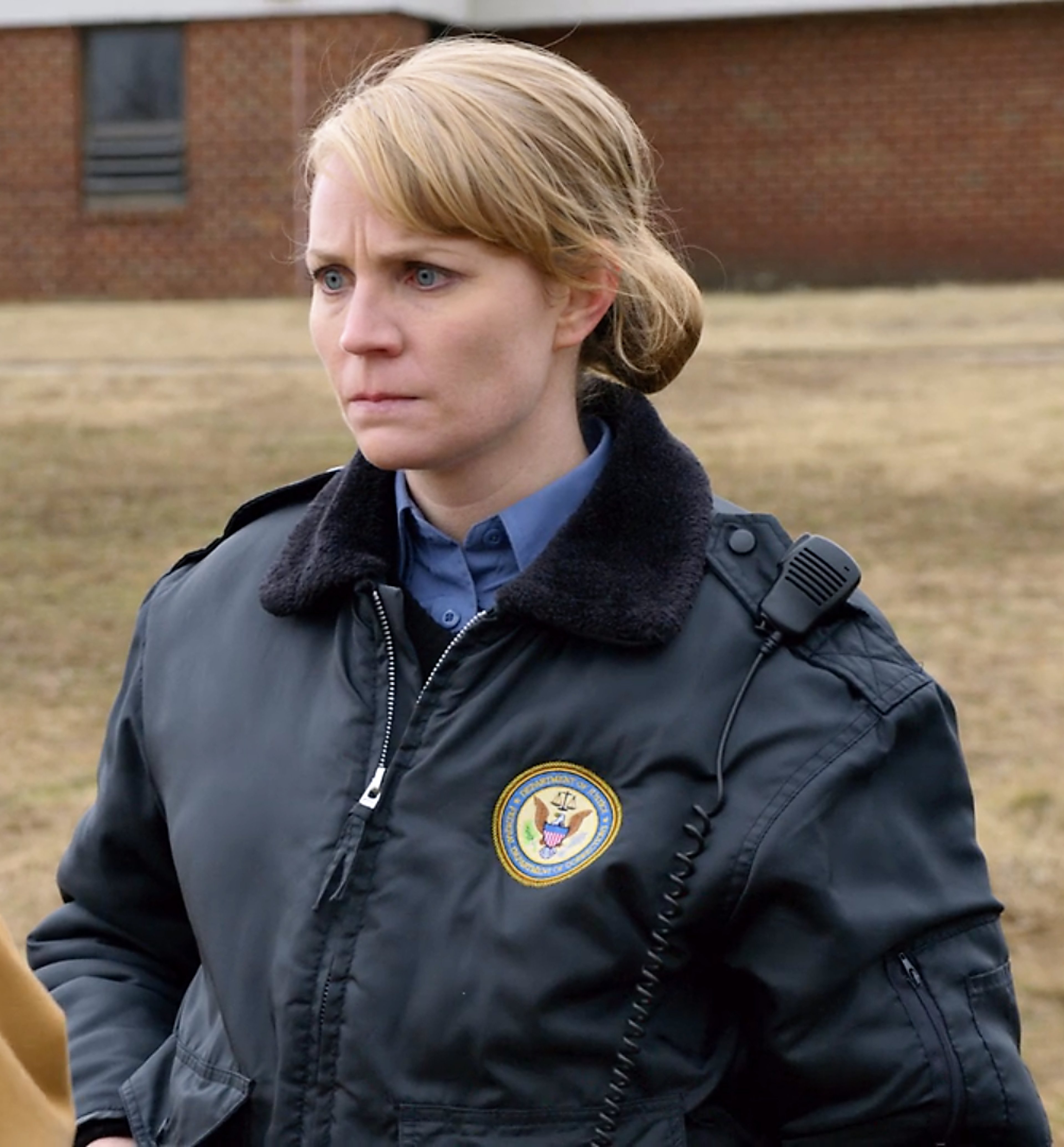 A woman in a black jacket with a patch on the sleeve standing outdoors