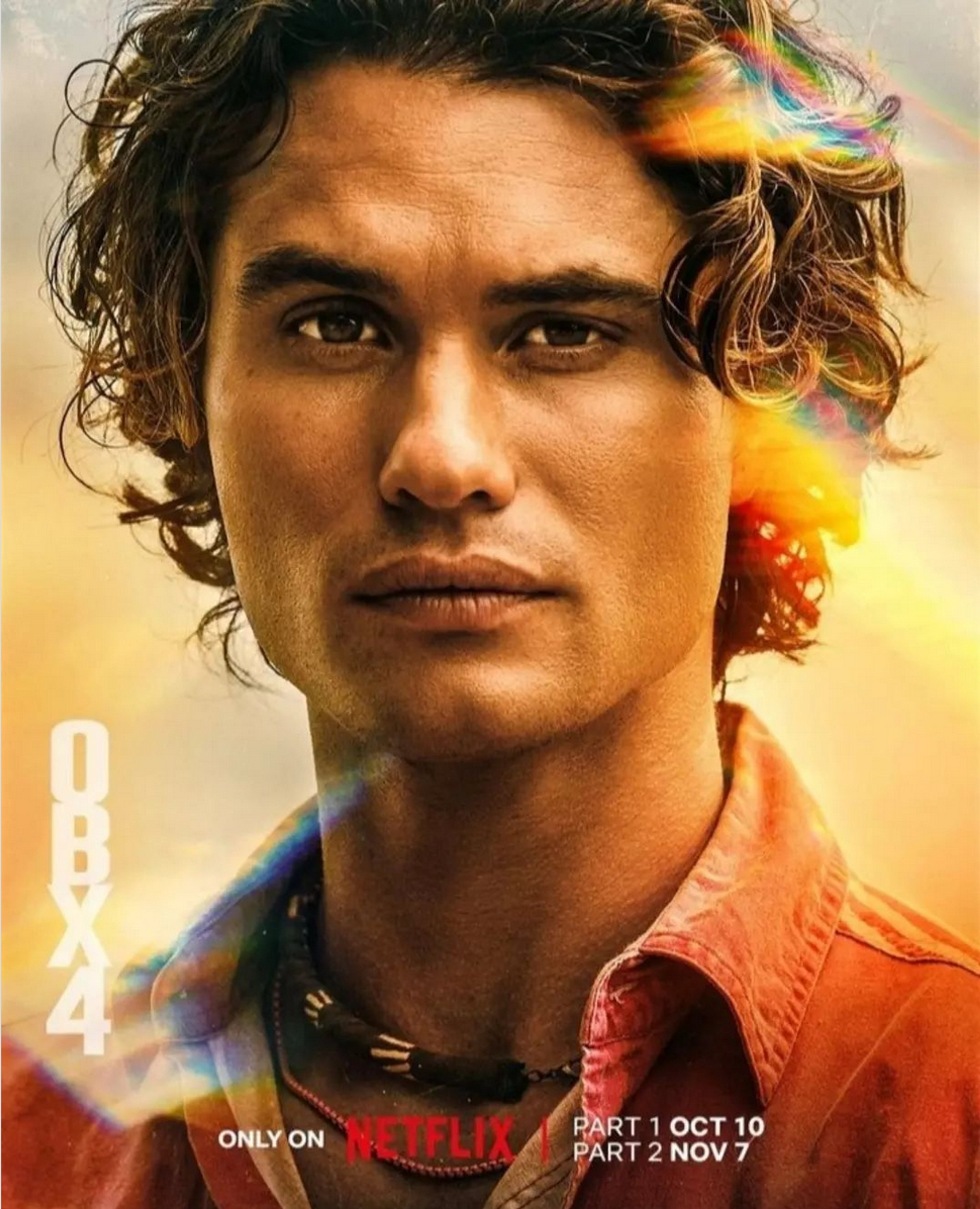 A young man with curly brown hair and a determined expression, wearing an orange shirt in an outdoor setting.