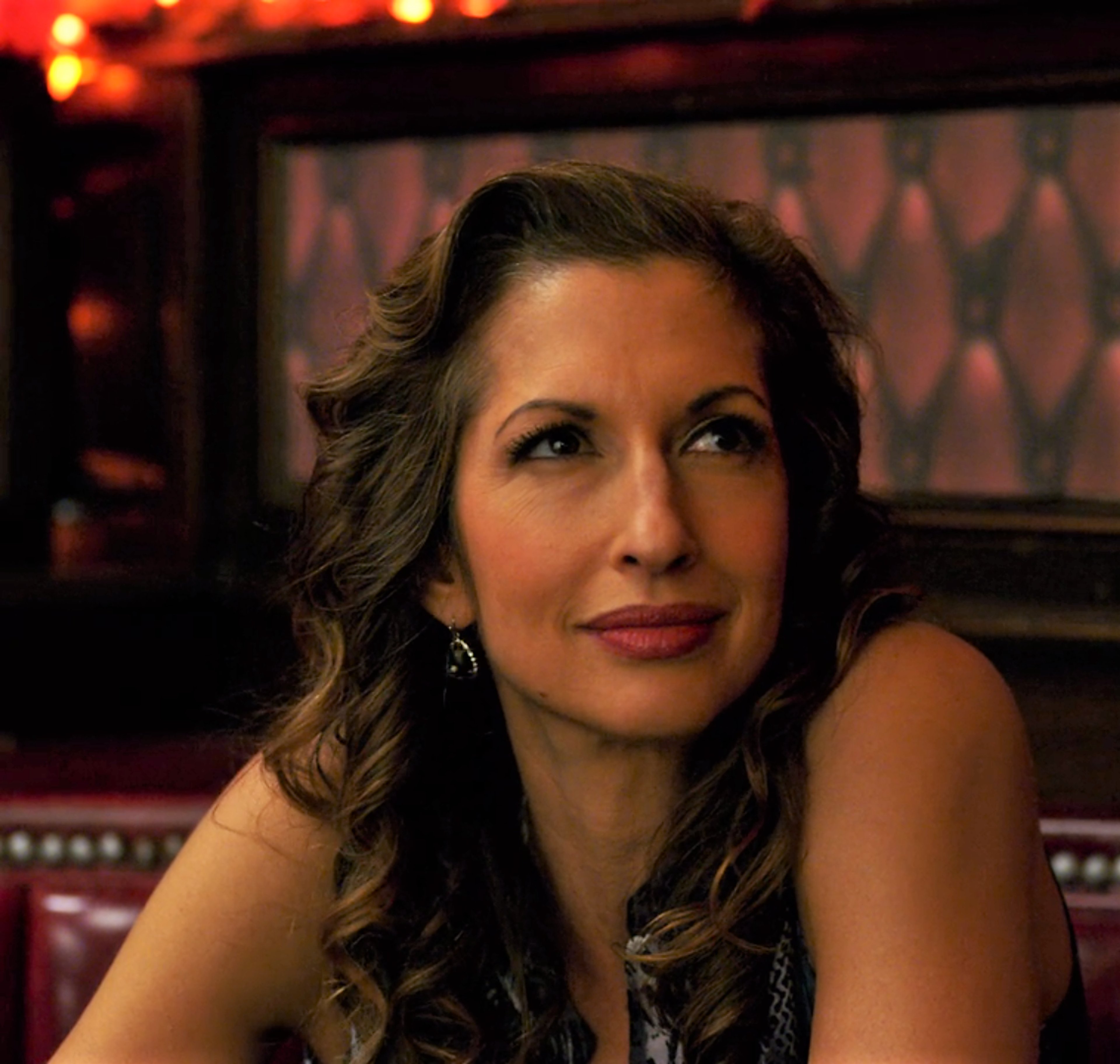 A woman with dark curly hair wearing a black dress in a dimly lit setting