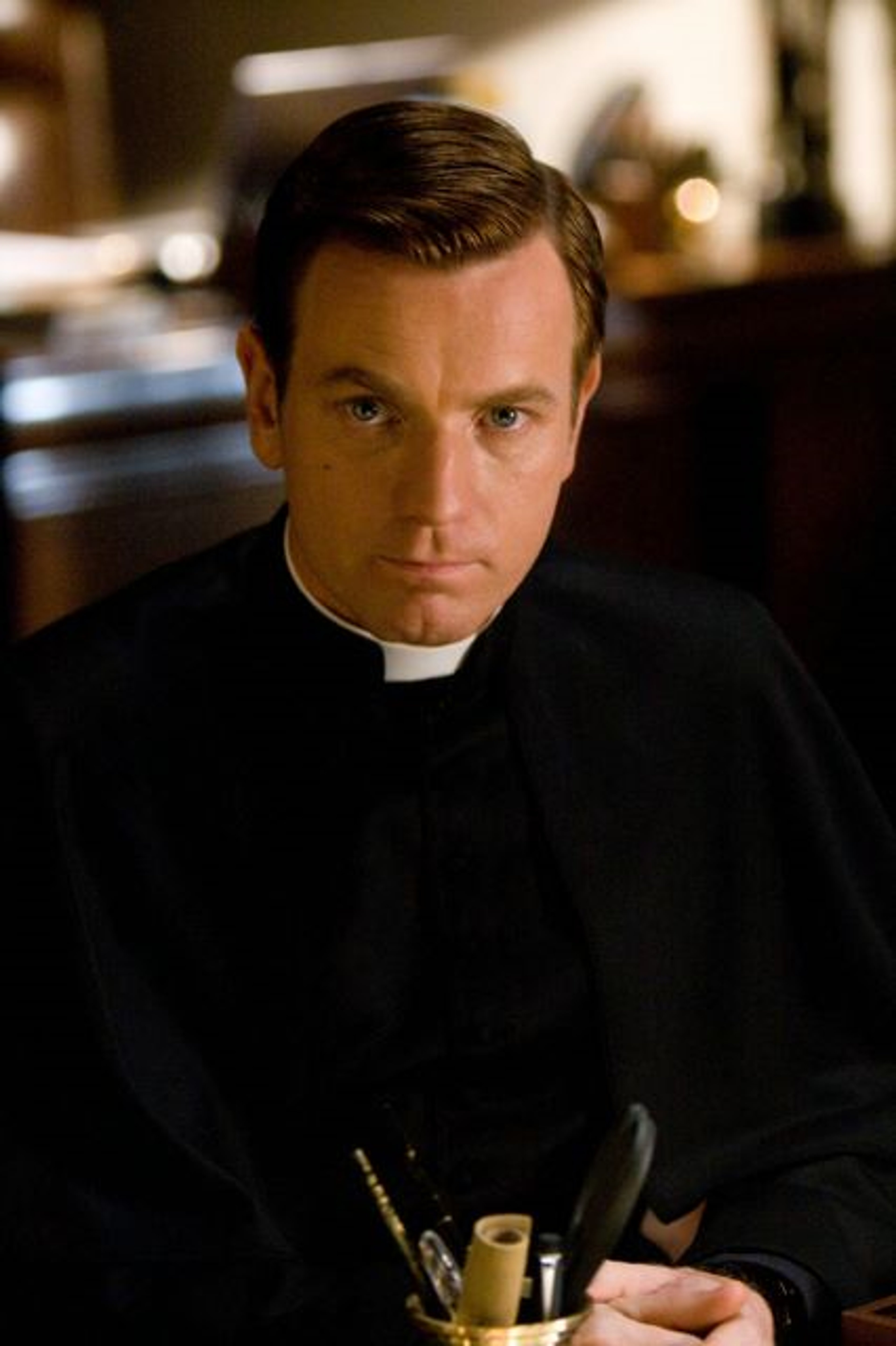A middle-aged man in a black clerical robe holding a religious item