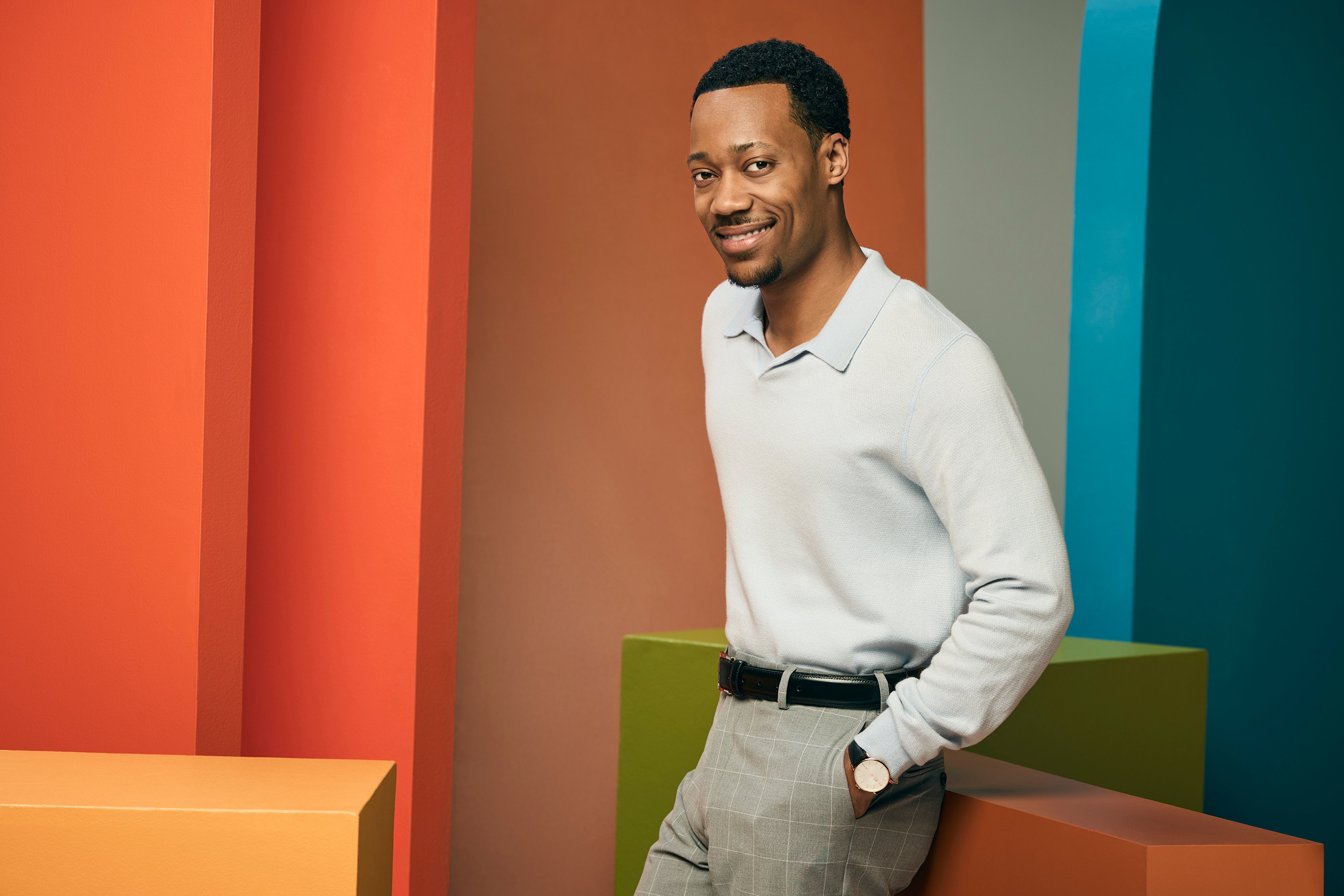A middle-aged Black man in a white shirt standing in front of a colorful background