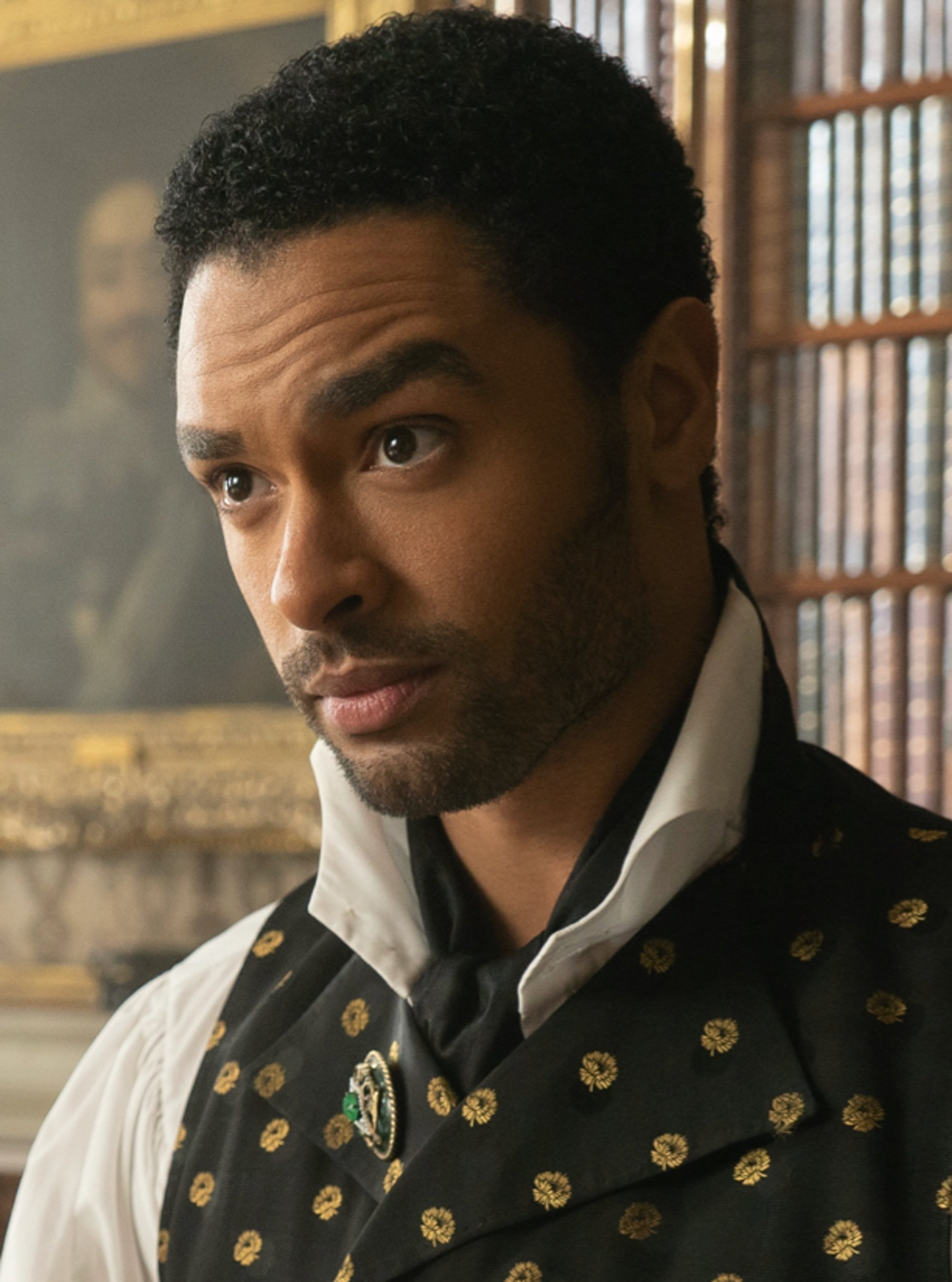 A man with dark skin and curly hair wearing a black and gold patterned jacket