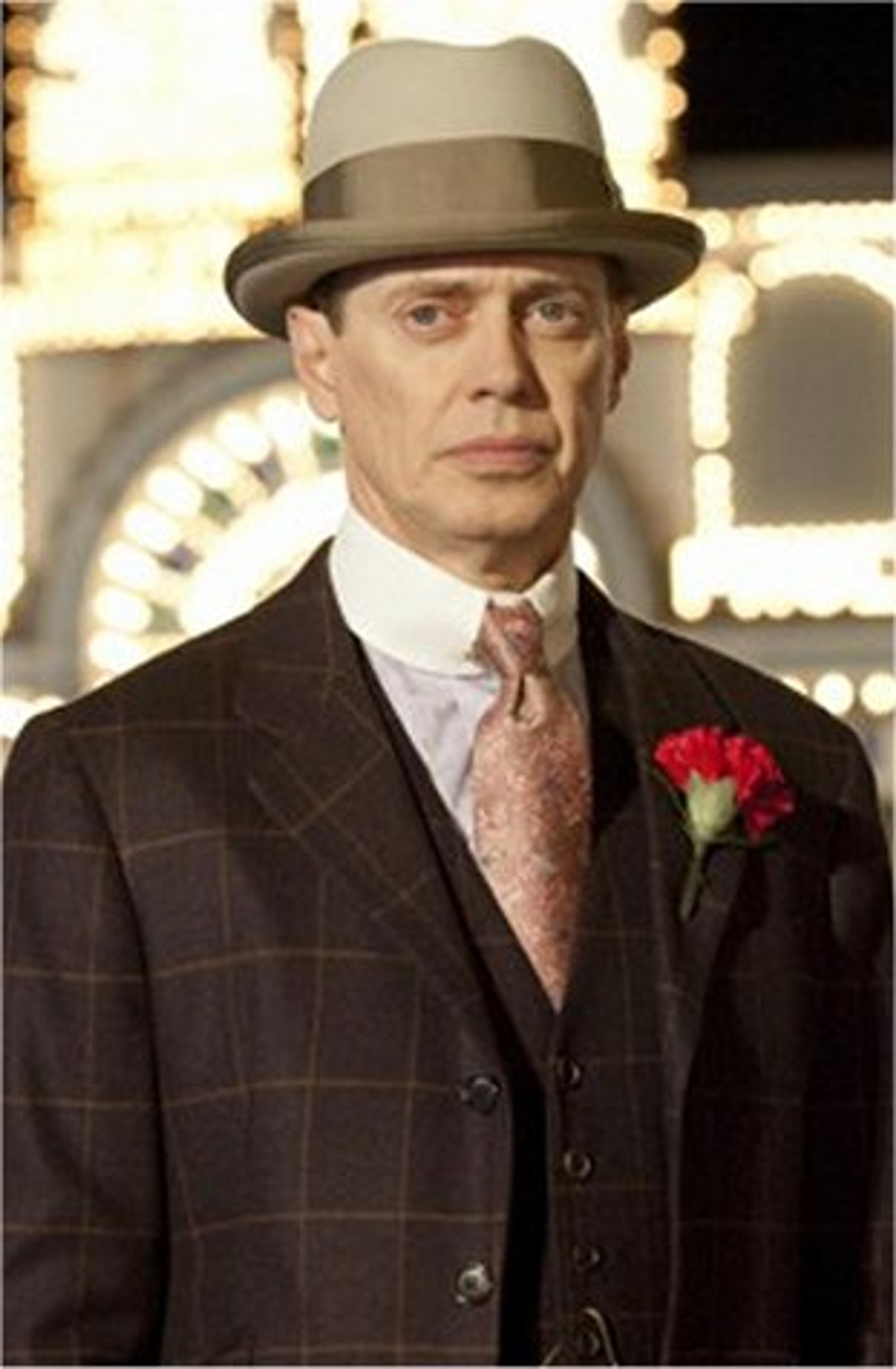A well-dressed older man in a suit and hat with a serious expression