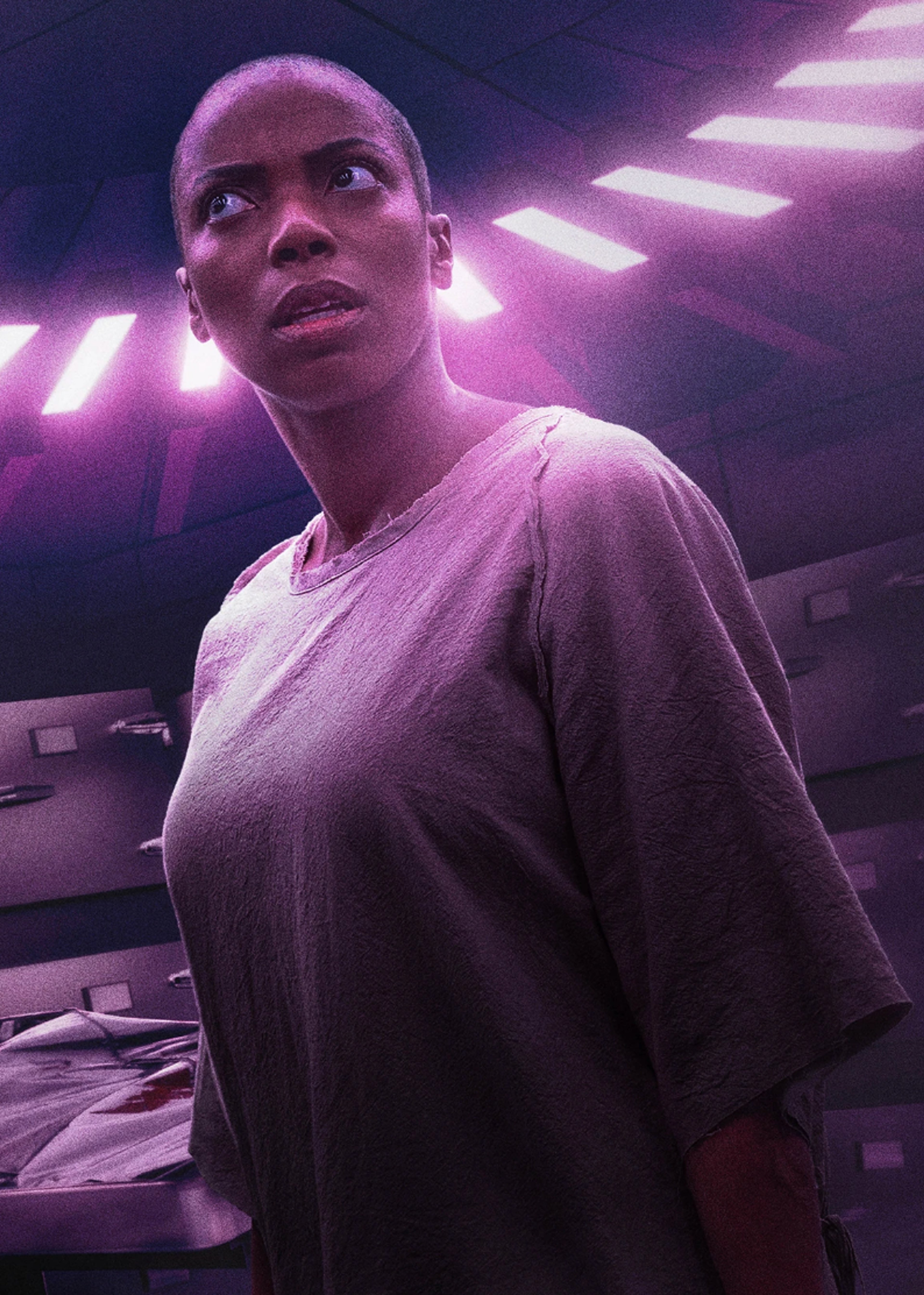 A confident-looking Black woman with short dark hair wearing a light pink shirt or dress, with dramatic pink and purple lighting behind her.