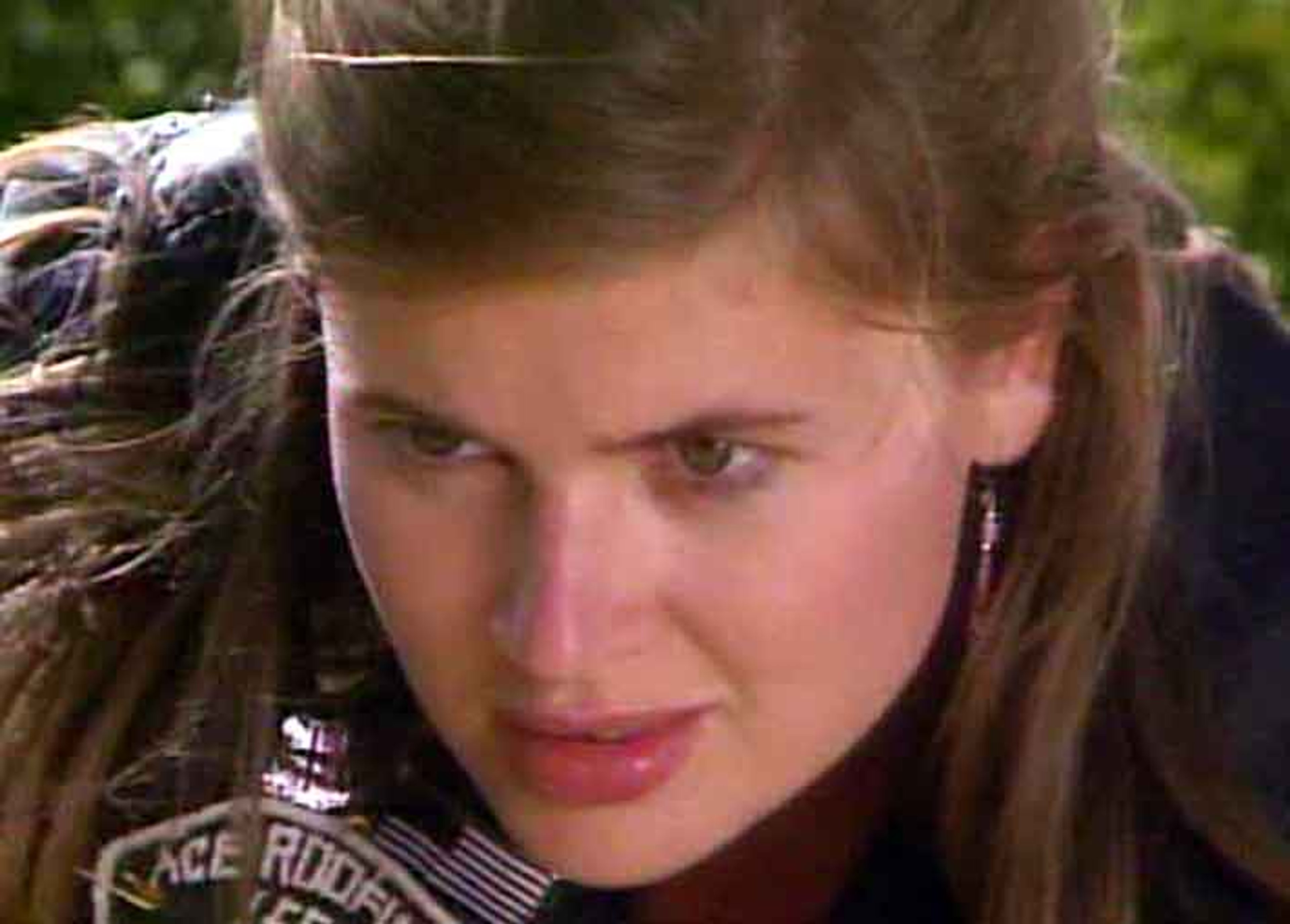 A young woman with short dark hair and a punk rock style, wearing a black leather jacket and looking serious.