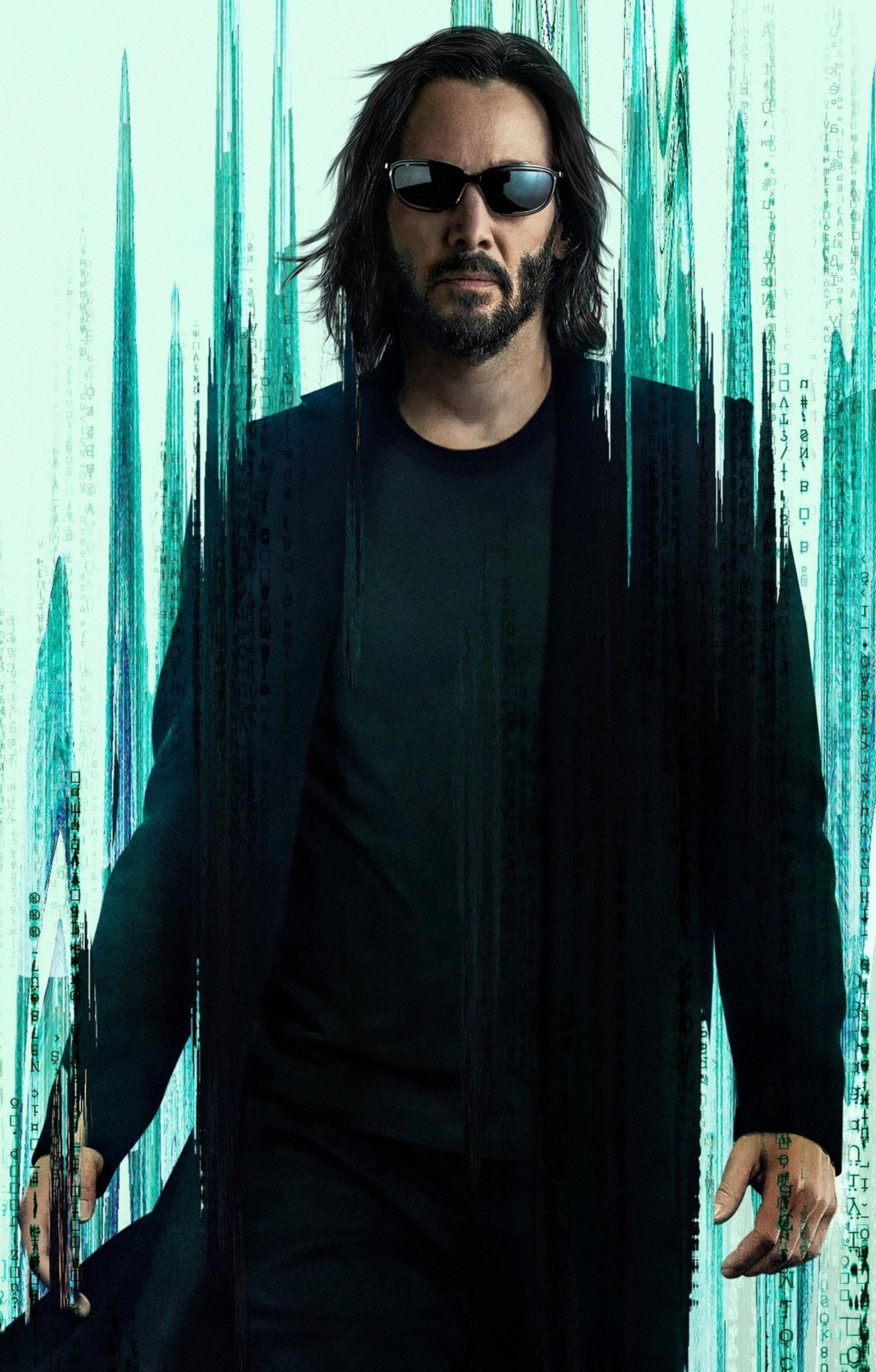 A man in a black suit with long dark hair and sunglasses standing in front of a blurred green and black background.