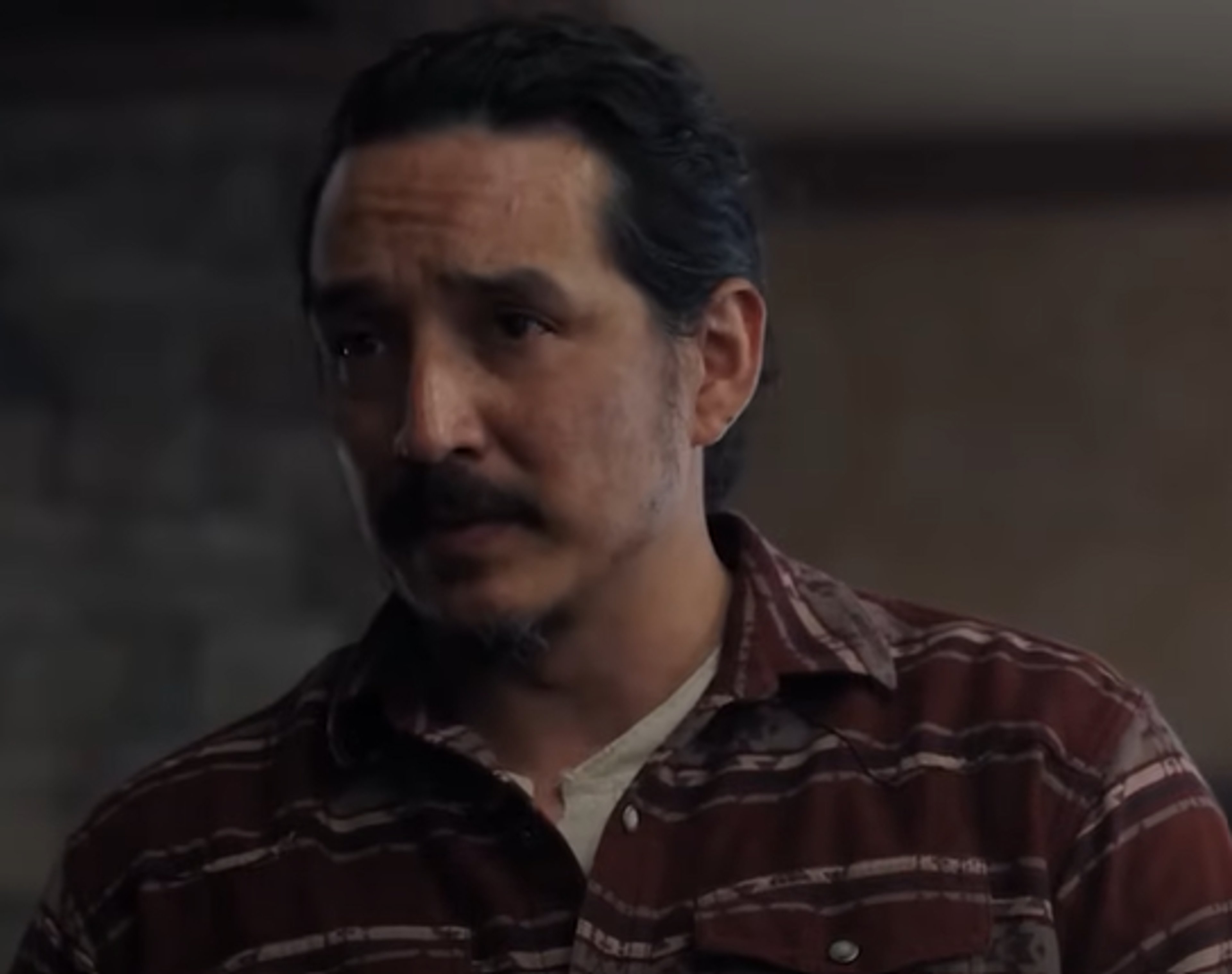 A middle-aged man with a serious expression wearing a plaid shirt