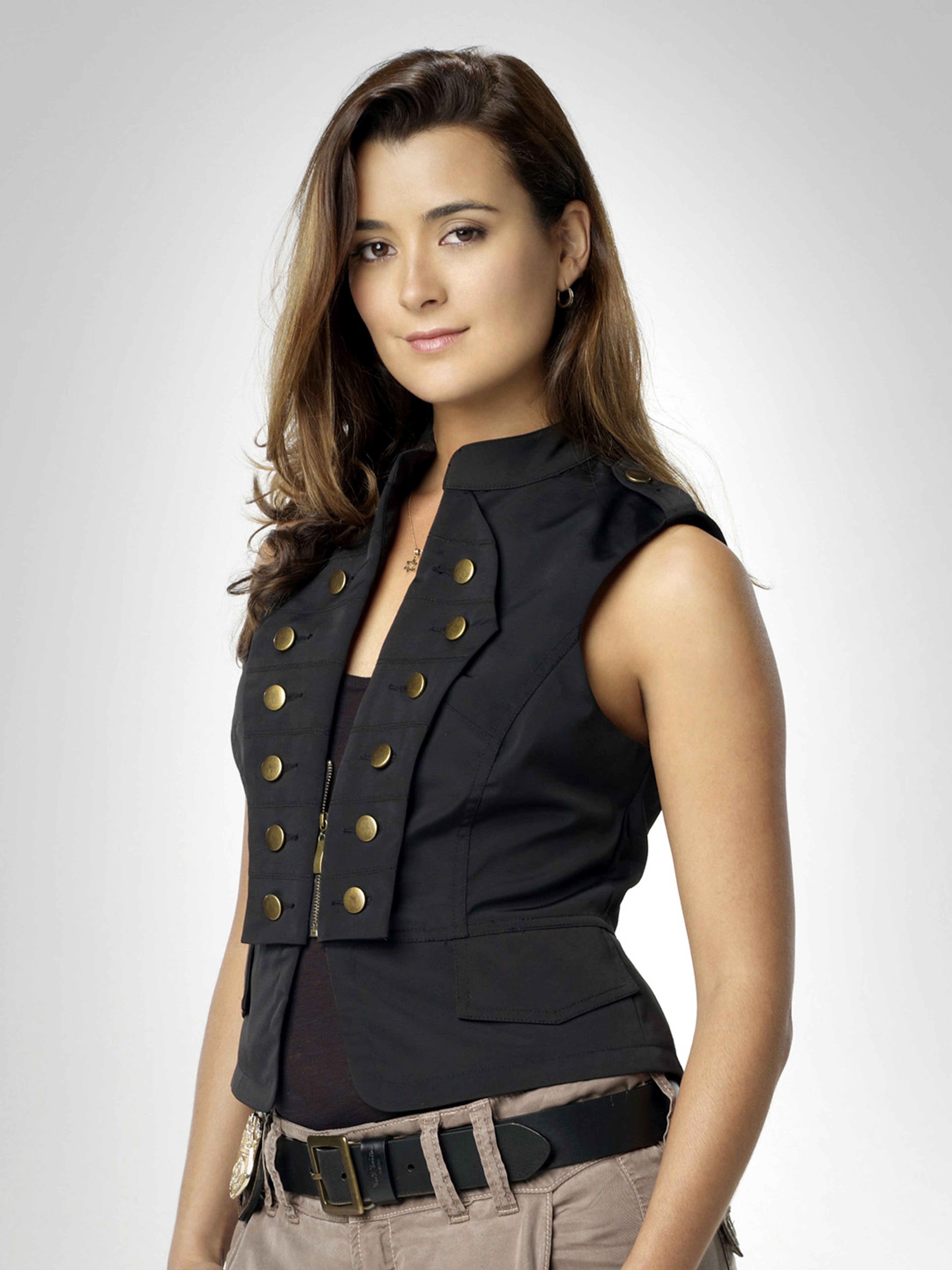 A woman with long brown hair wearing a black sleeveless top with gold buttons