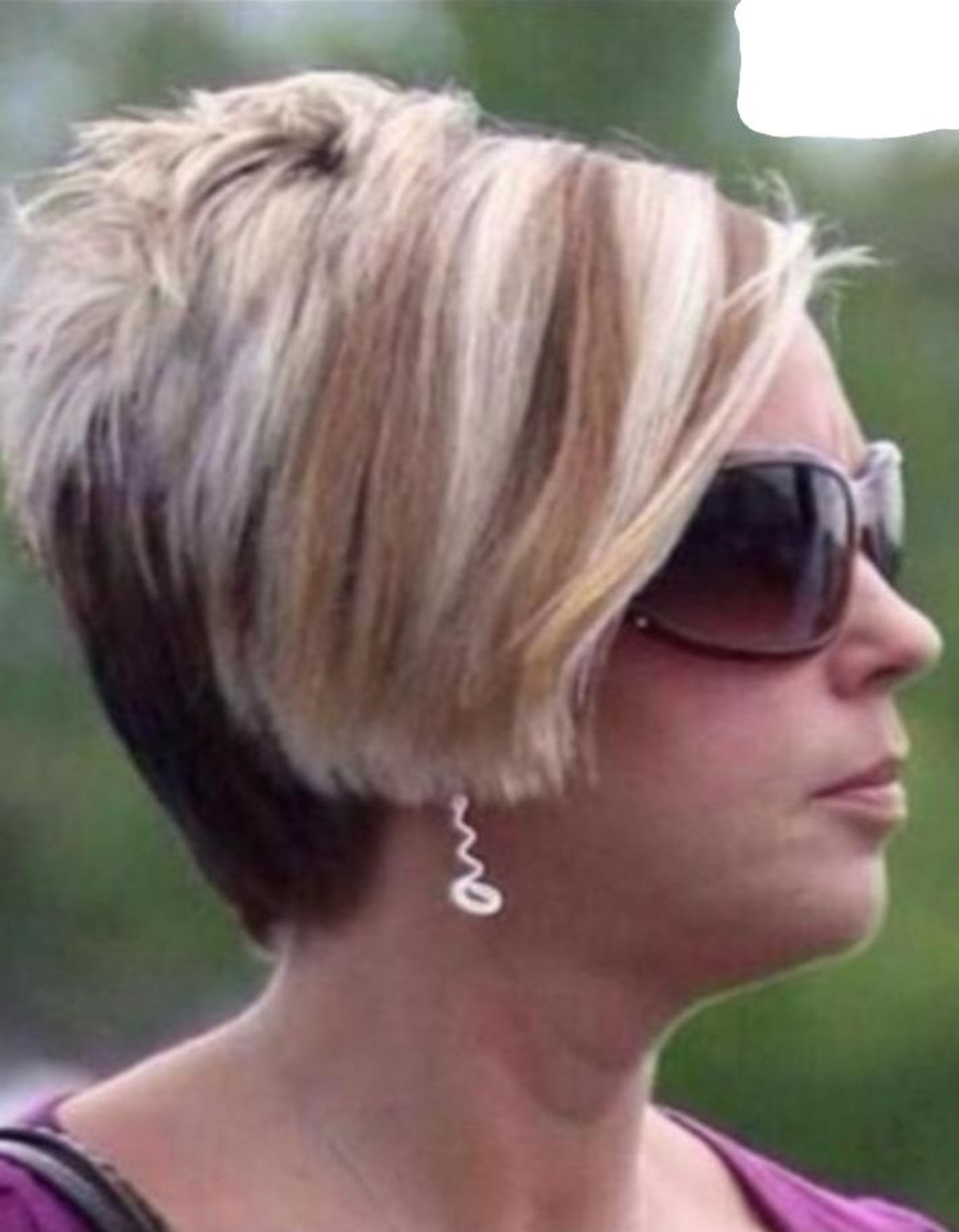 A middle-aged white woman with short blonde hair and sunglasses, wearing a pink top and looking confrontational.