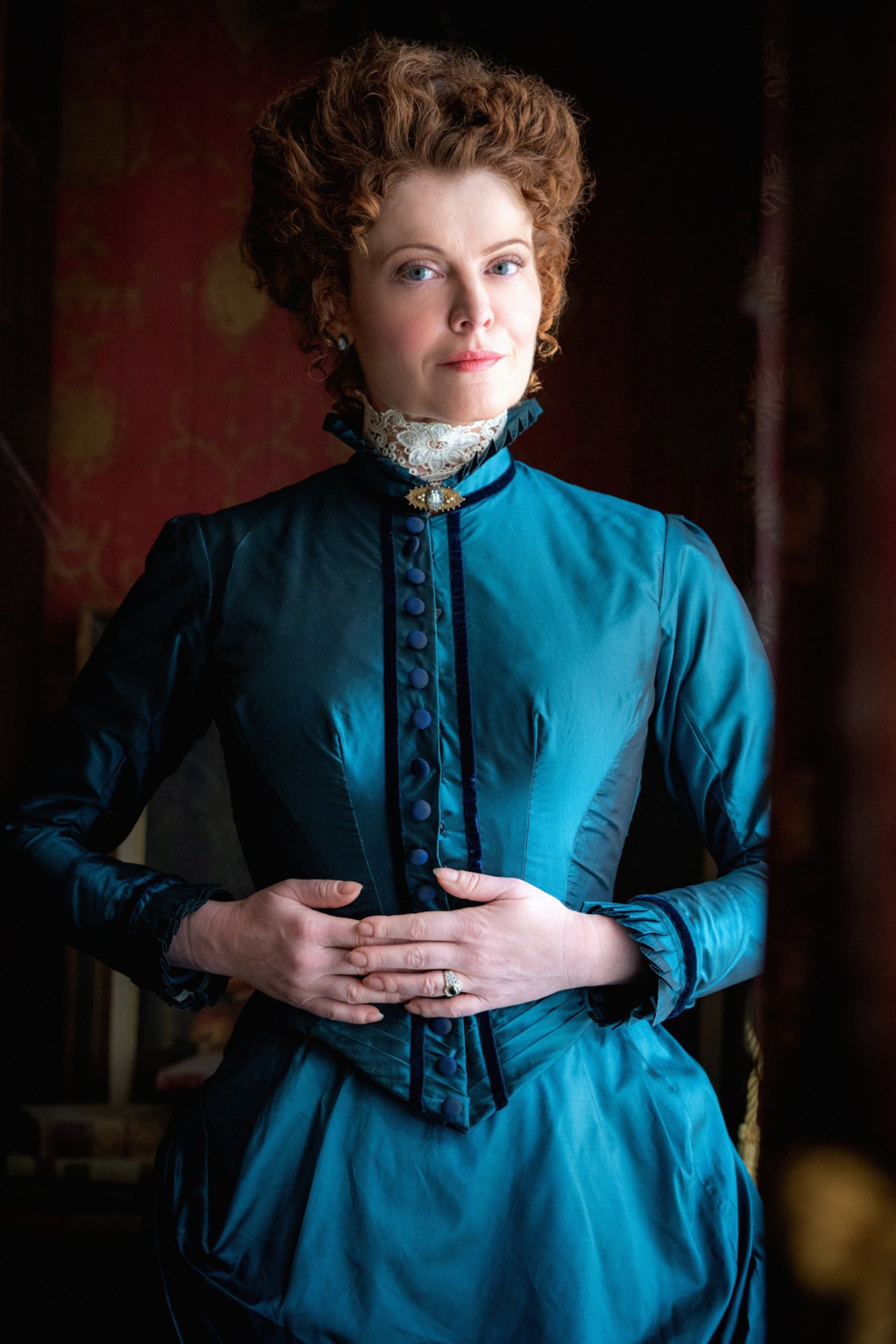 A woman in a teal Victorian dress with a serious expression