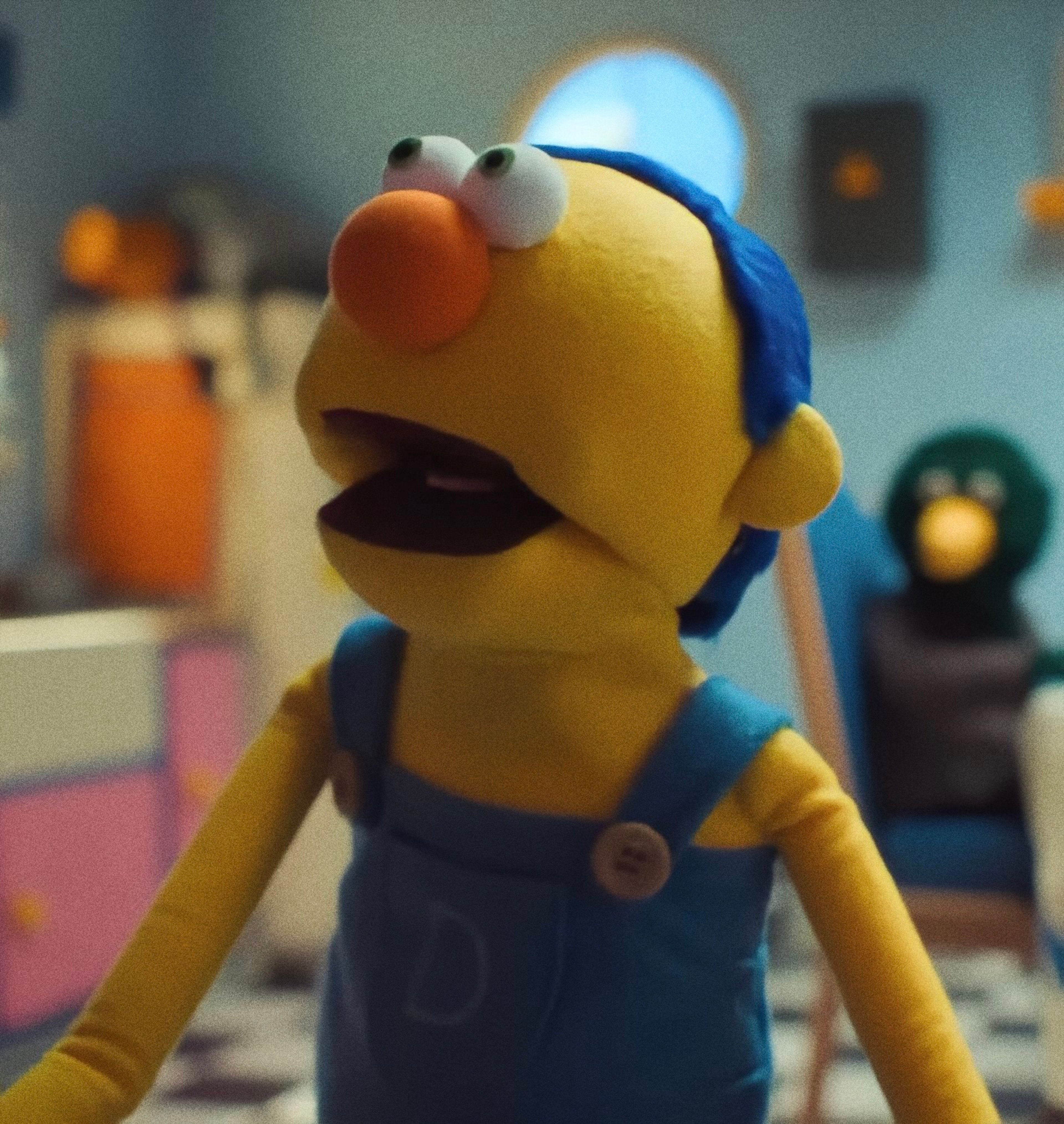 A detailed puppet character with a yellow body, green eyes, and neatly combed hair, wearing a blue outfit and displaying an intellectual, analytical expression.