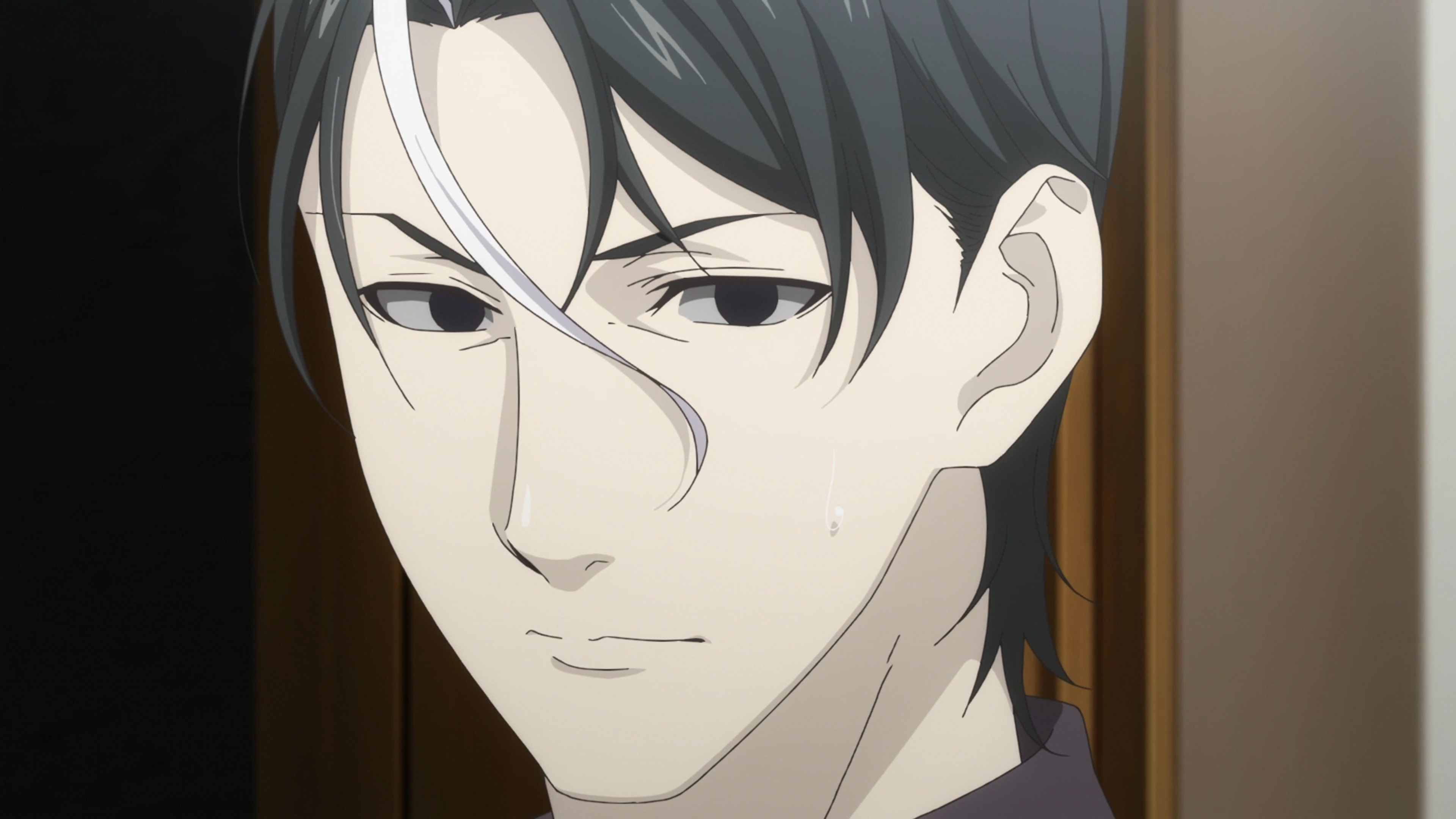 A serious-looking man with black hair and a white streak