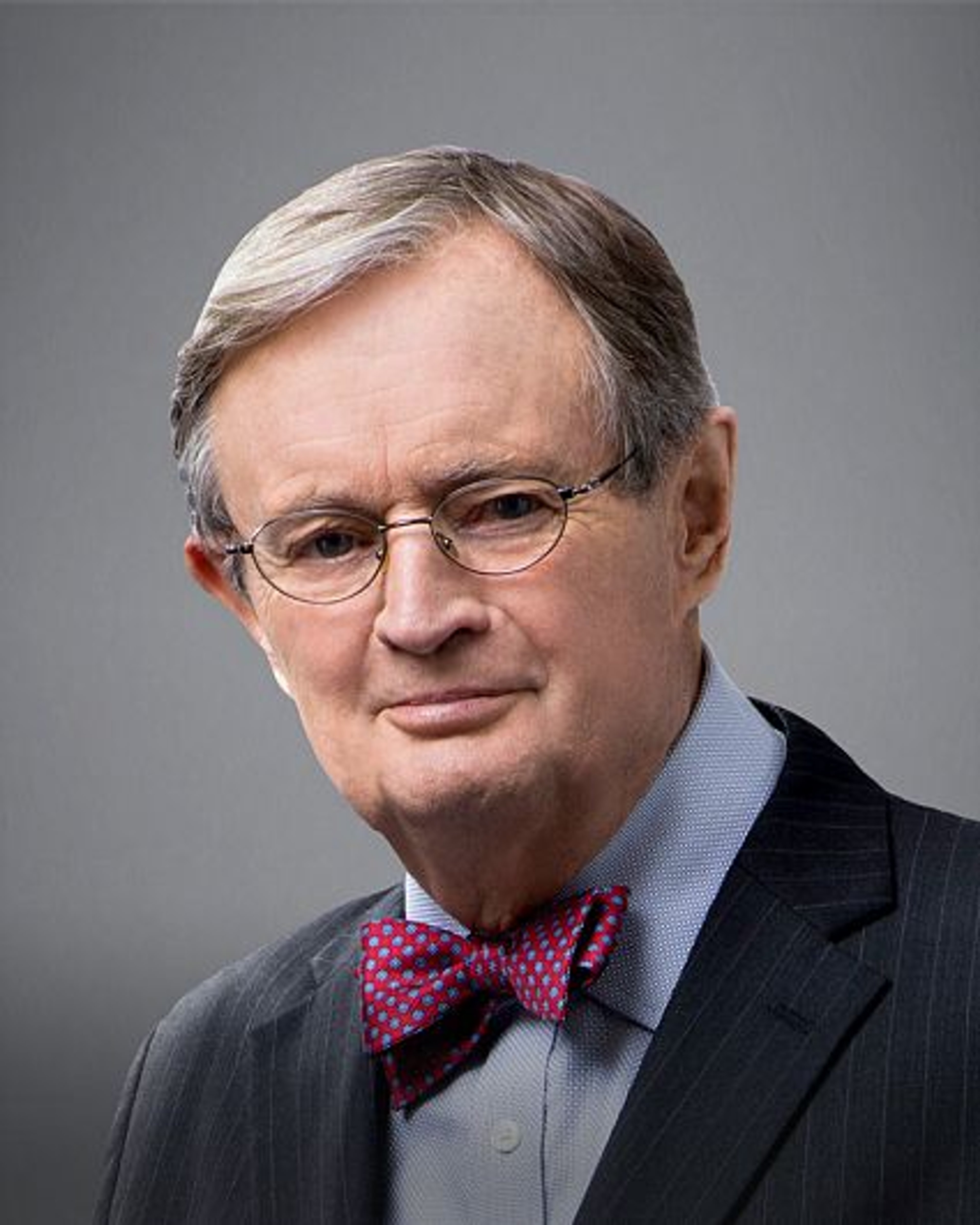 An older man with gray hair and glasses, wearing a suit and bow tie, with a warm, grandfatherly expression.