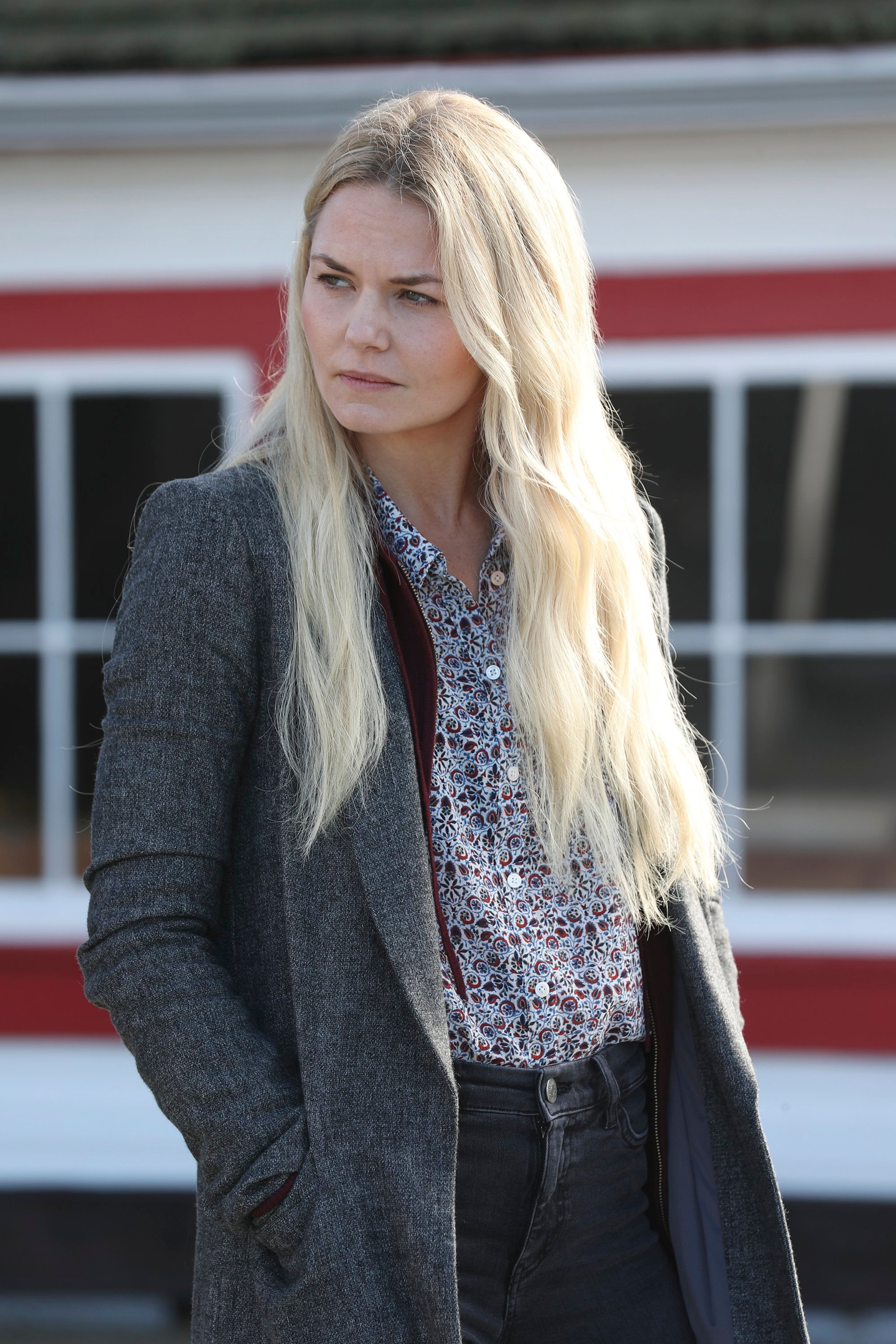 A woman with long blonde hair wearing a gray coat standing outside