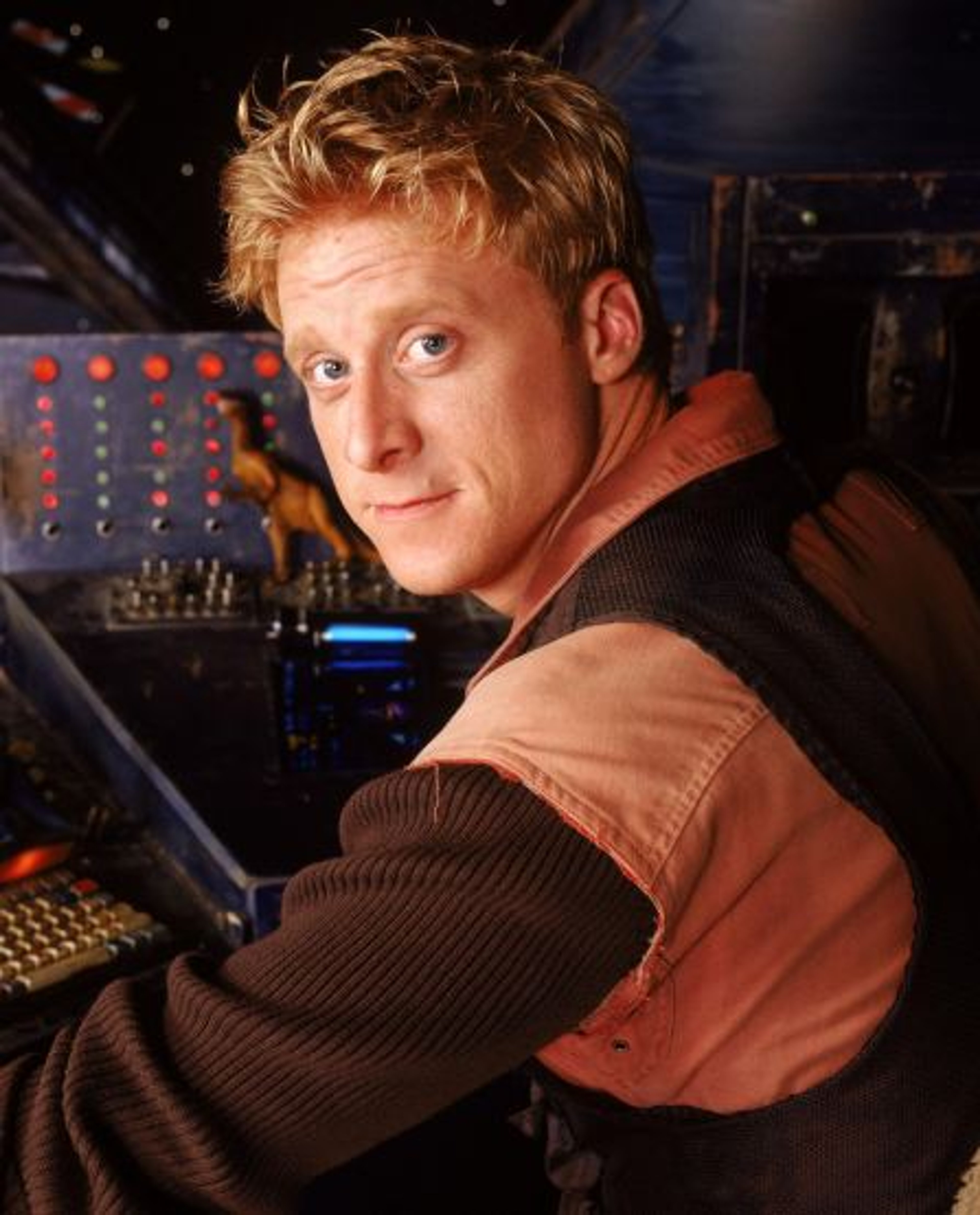 A man with short blond hair and a beard sitting at a control panel