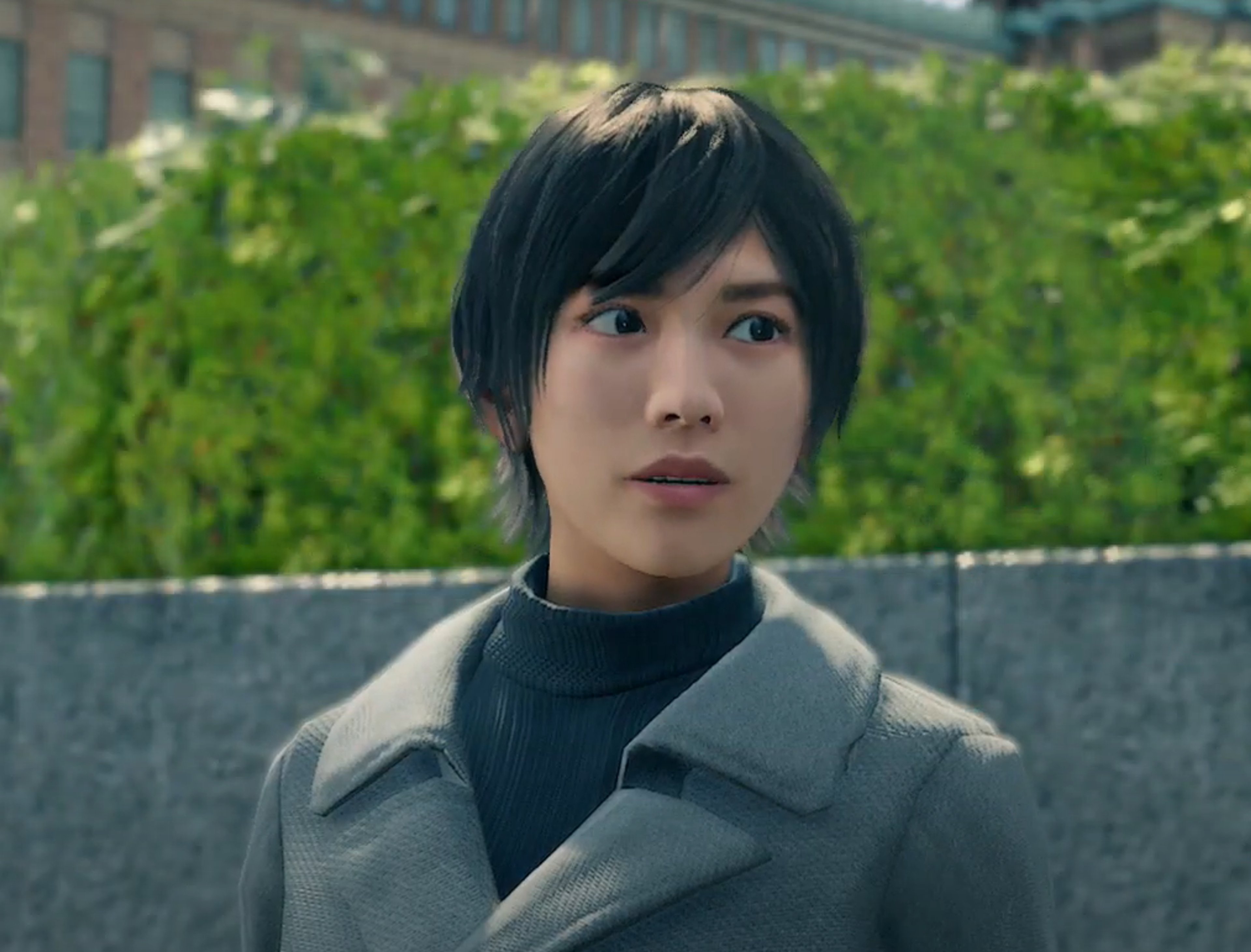 A young woman with short, dark hair wearing a light-colored coat and looking serious.