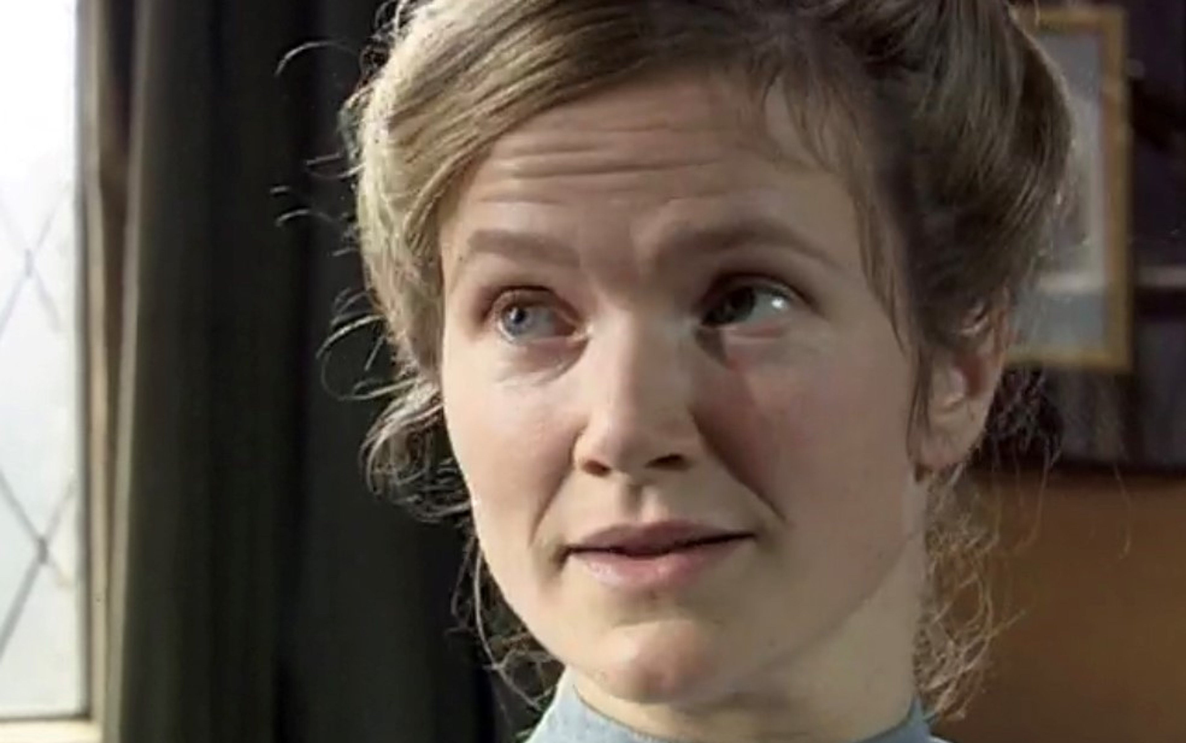 A middle-aged woman in a nurse's uniform with a serious expression