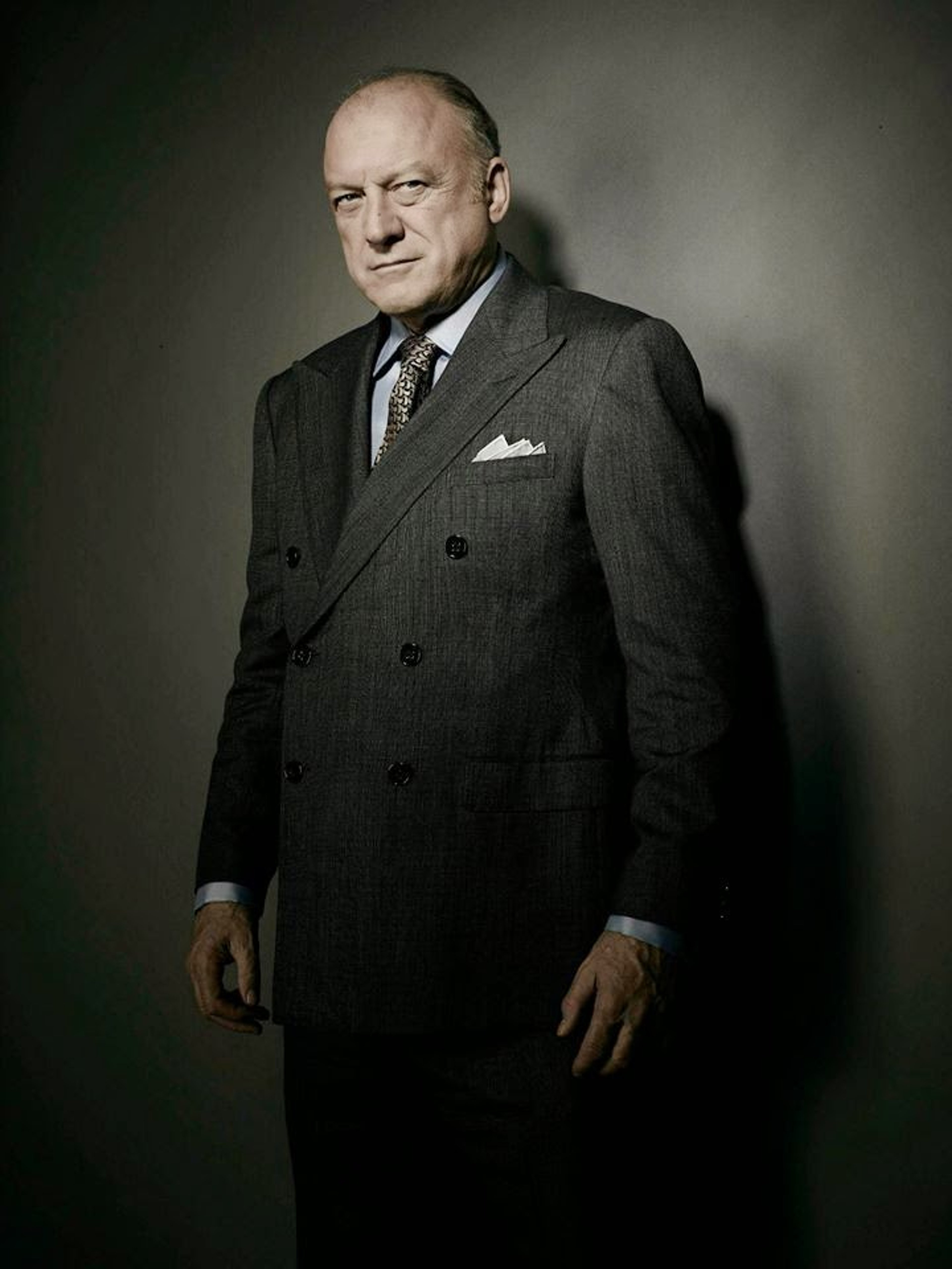 A middle-aged man in a dark suit and tie, with a serious expression