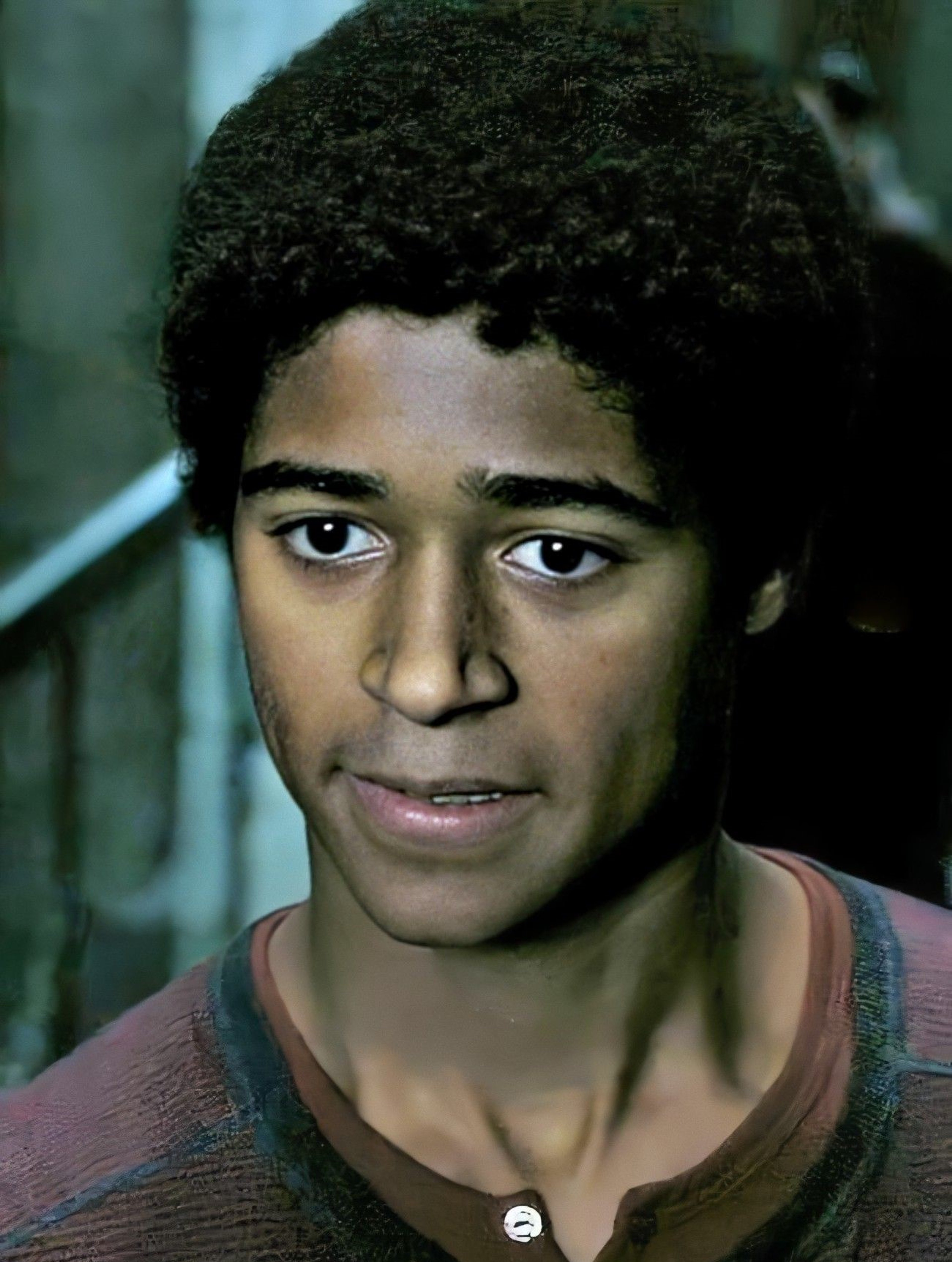 A young Black man with curly dark hair and a serious expression