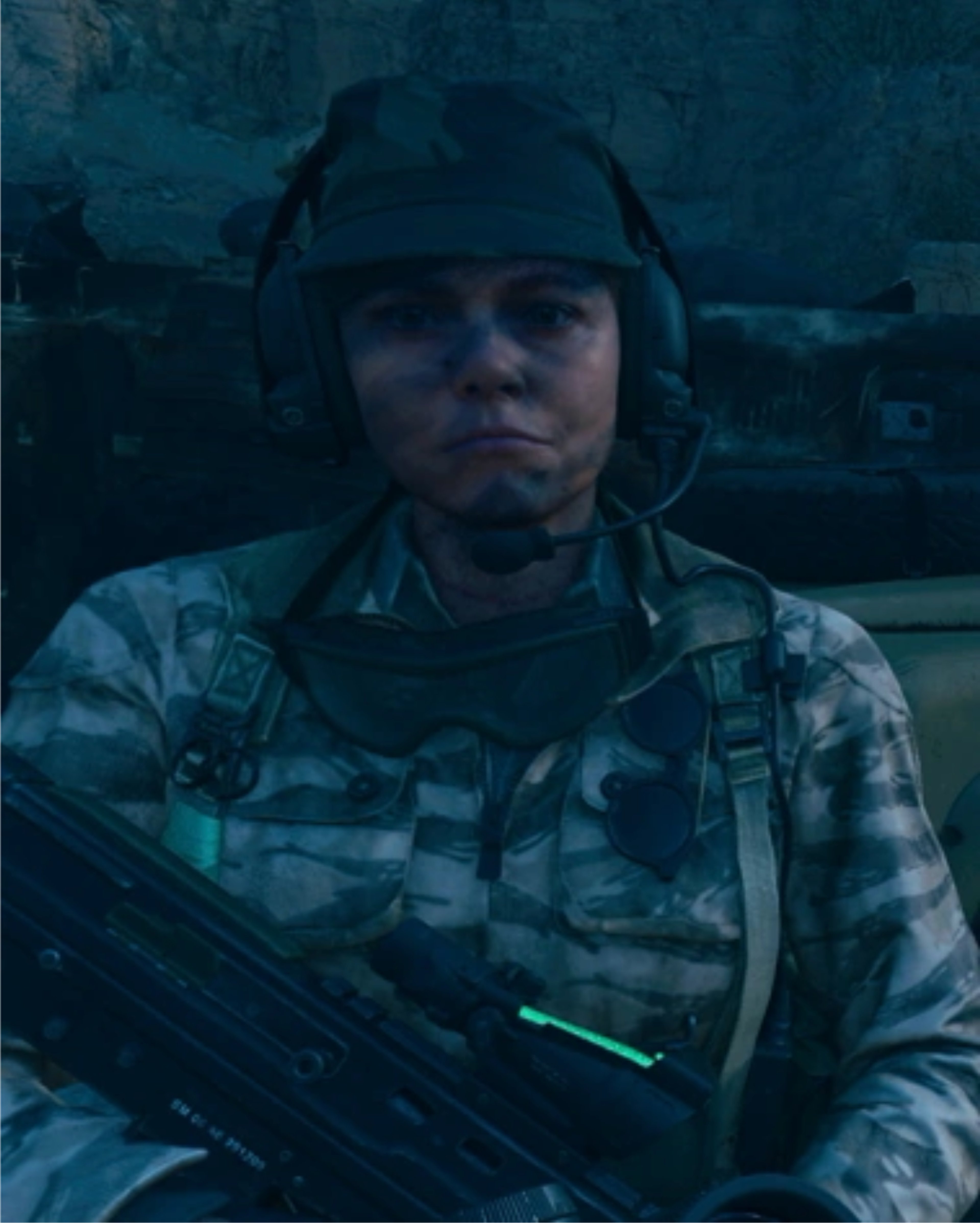 A young woman in military gear holding a firearm with a serious expression