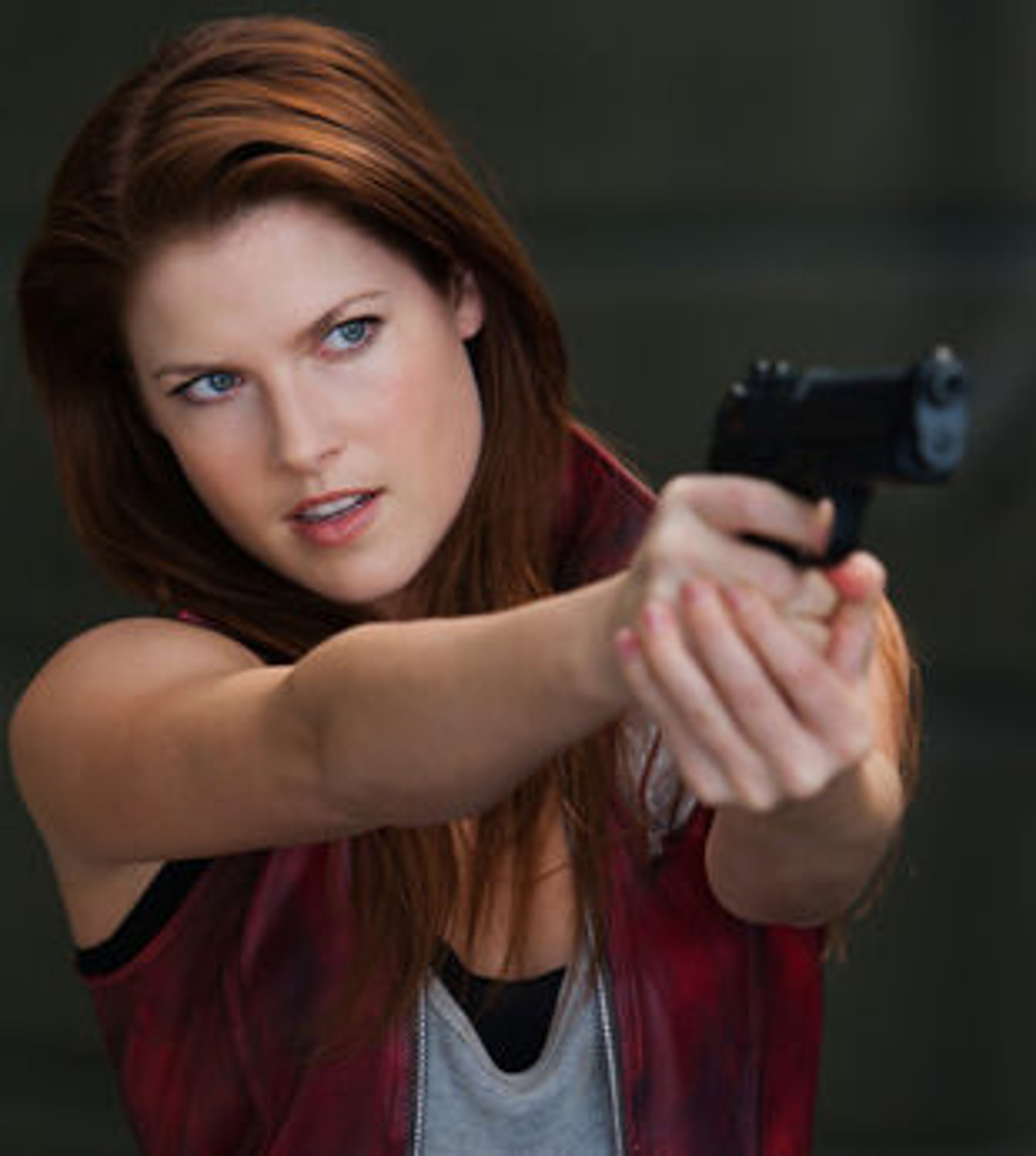 A woman with long reddish-brown hair wearing a red leather jacket and holding a handgun