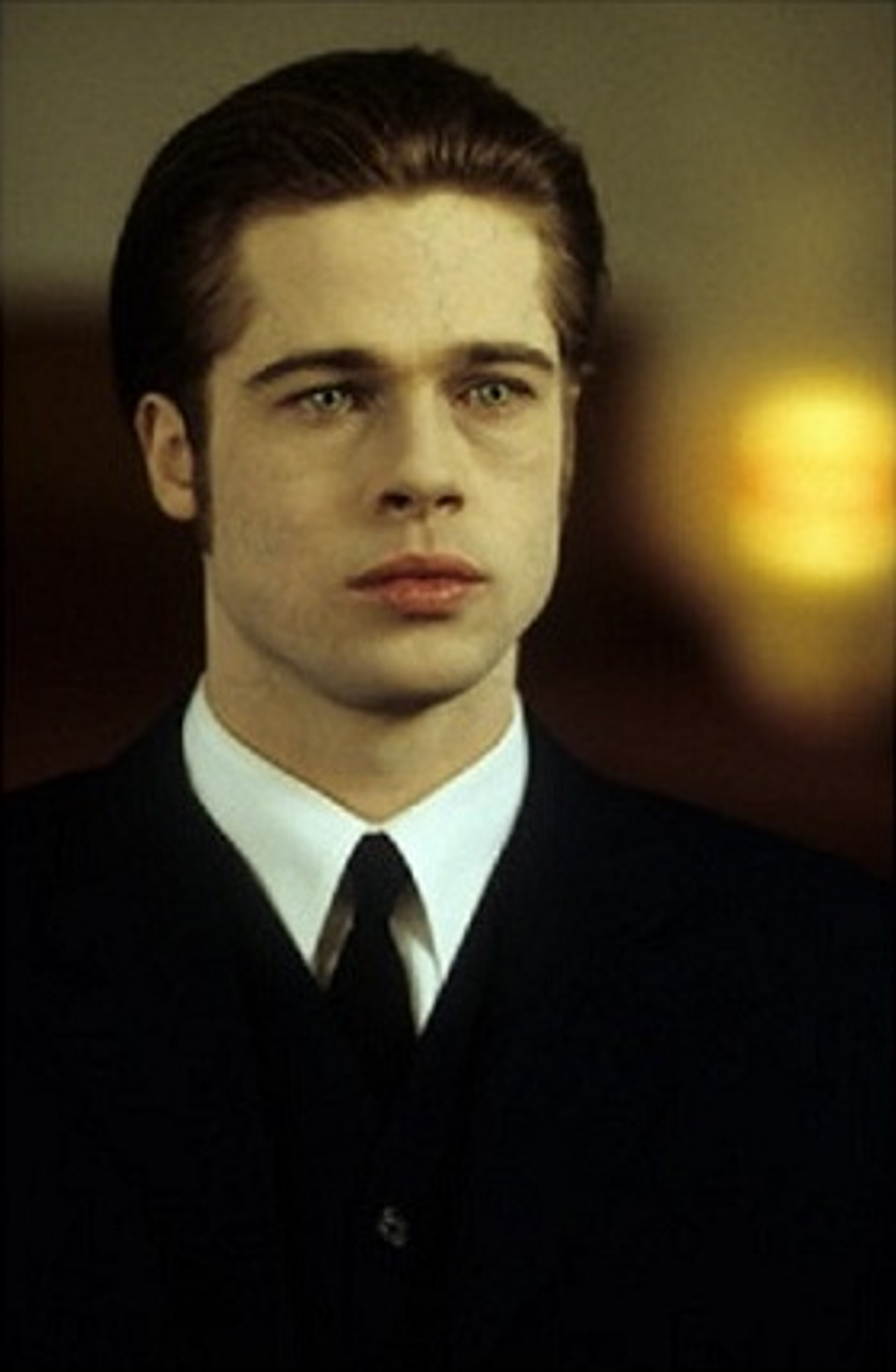Portrait of a young man with pale skin, dark hair, and green eyes wearing a black suit and tie.