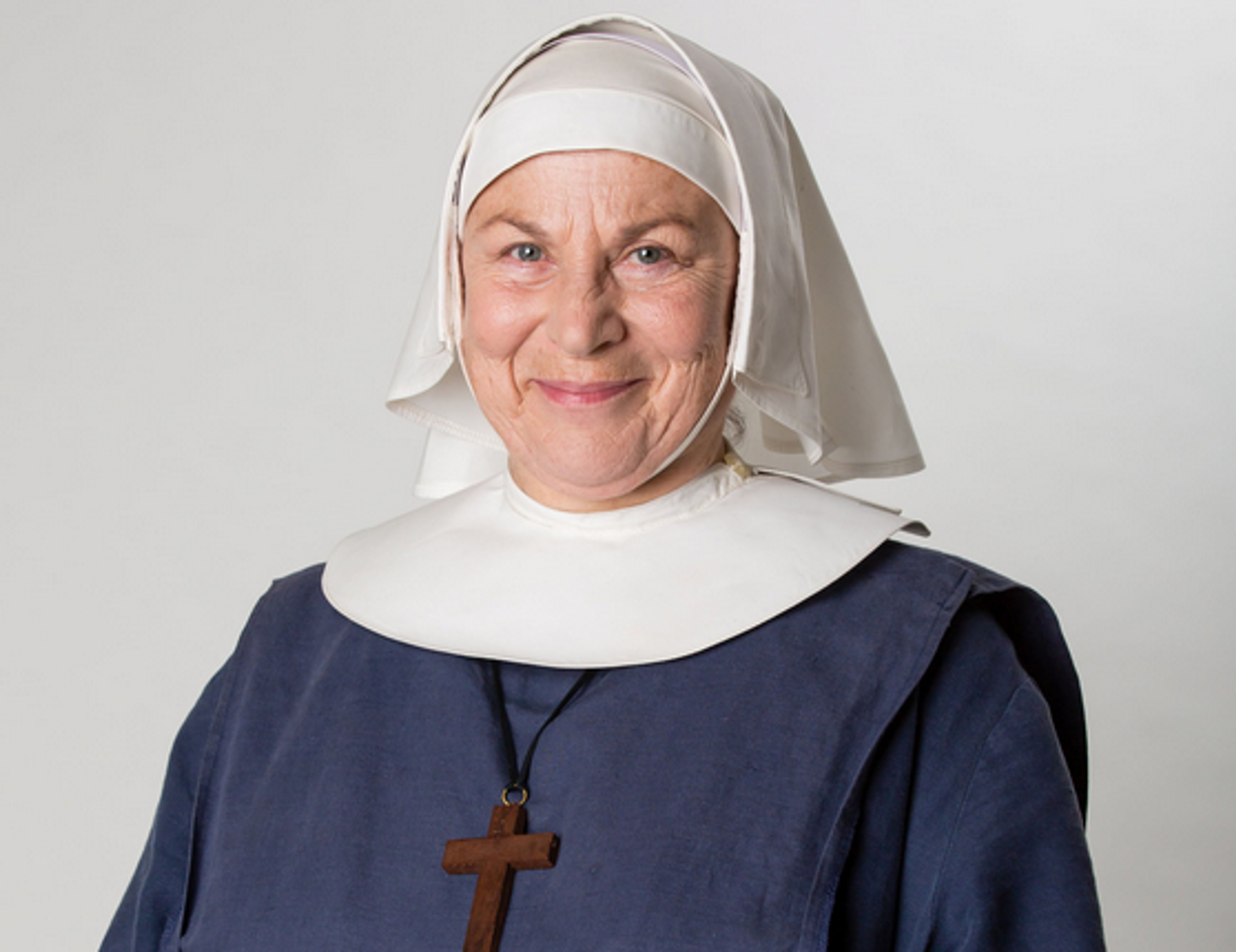 An elderly nun with a stern expression wearing a white coif and dark blue habit