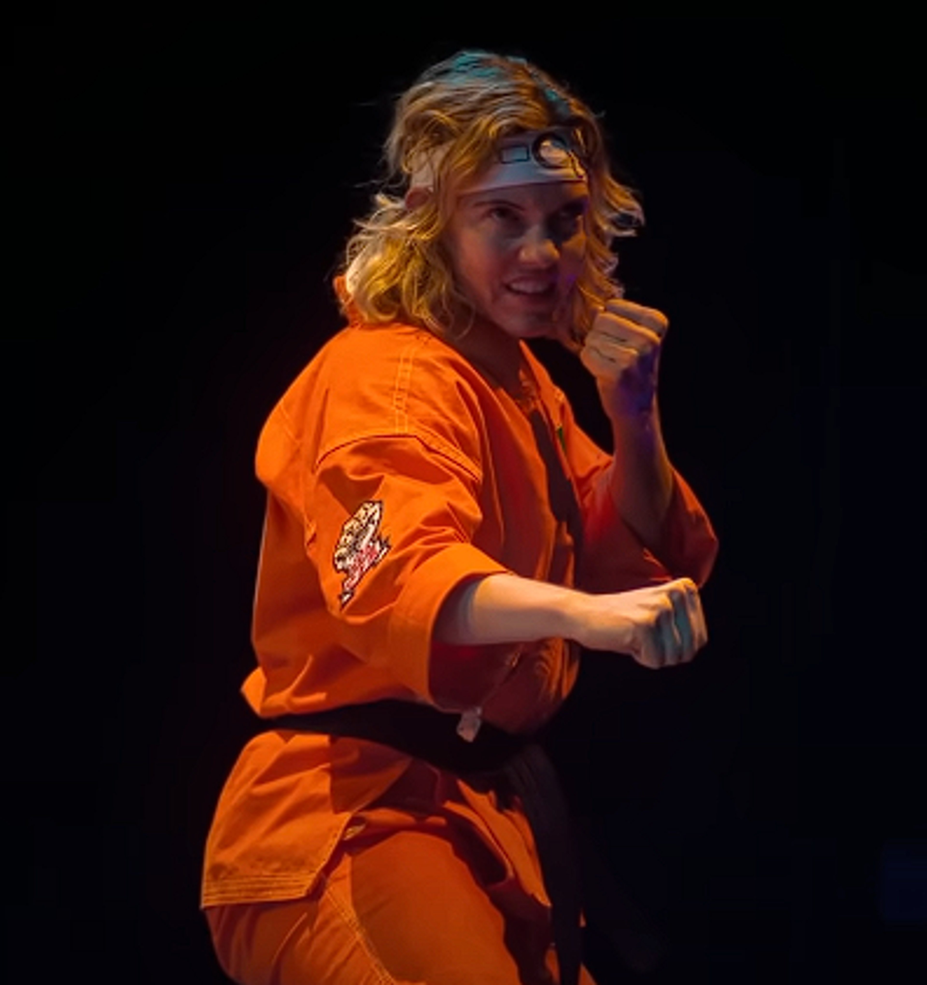 A young woman in an orange martial arts uniform in a fighting stance