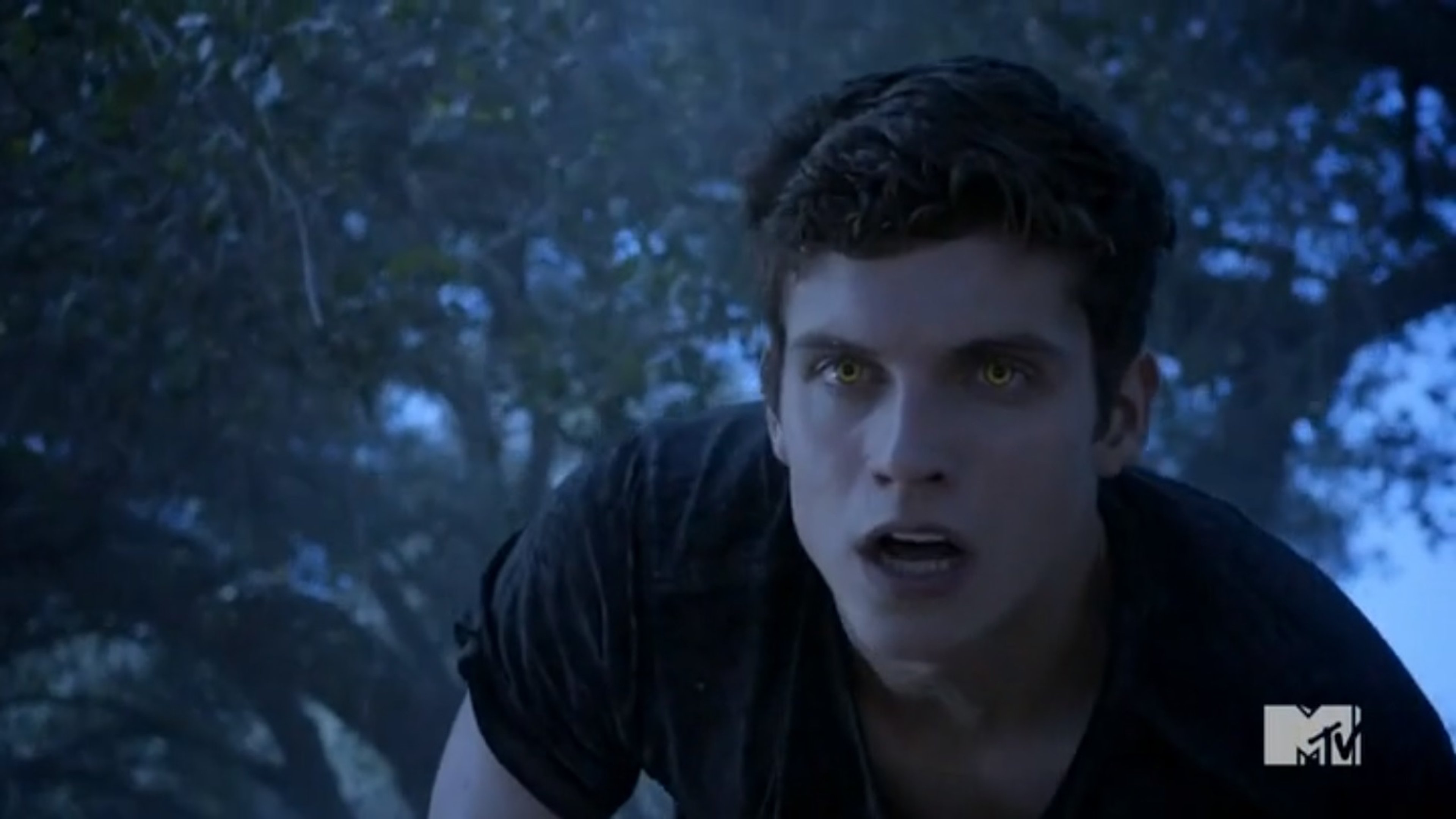 A young man with a serious expression in a dimly lit outdoor setting