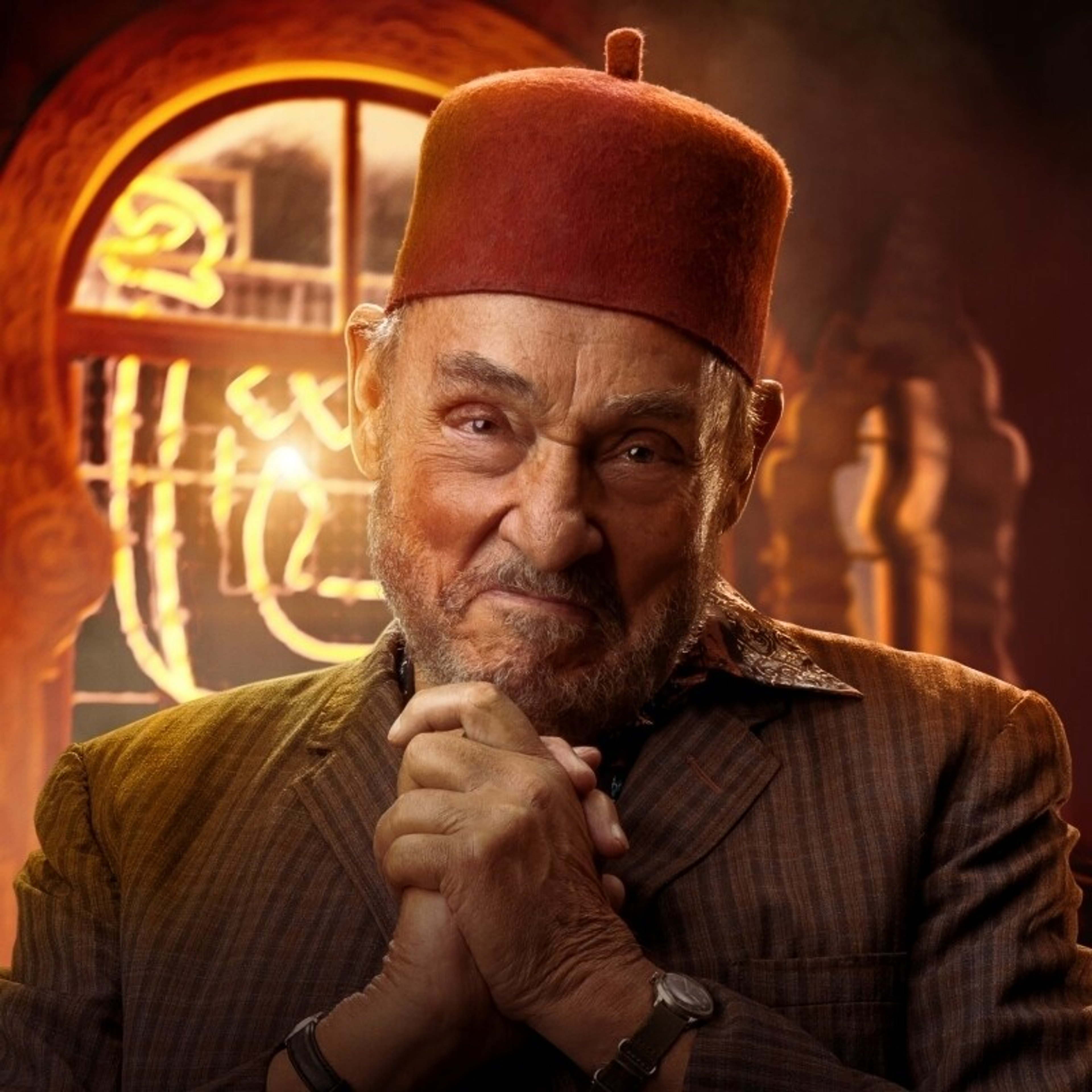 An older Middle Eastern man with a red fez hat and yellow robe, smiling warmly.