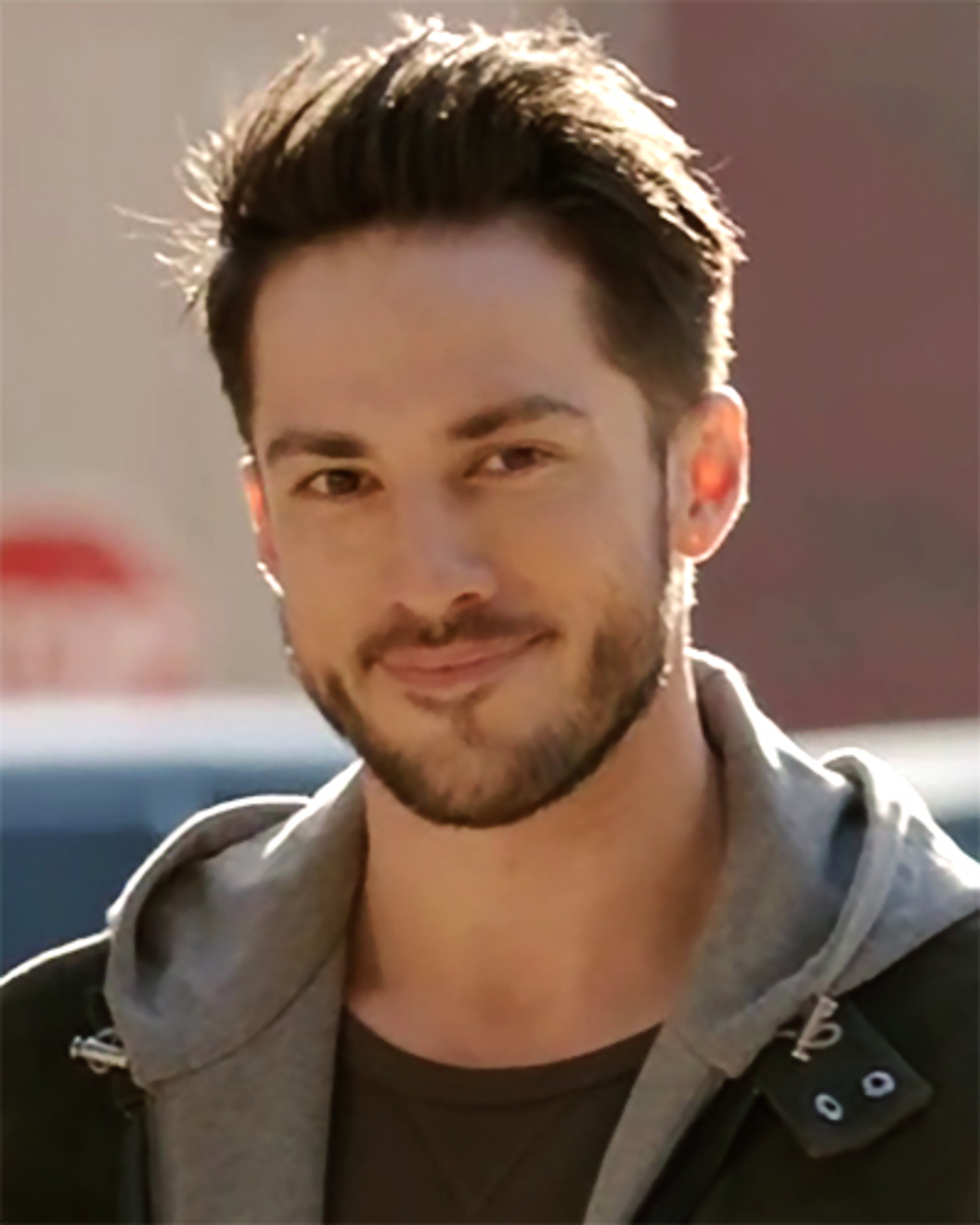 A young man with short dark hair and facial hair wearing a gray jacket