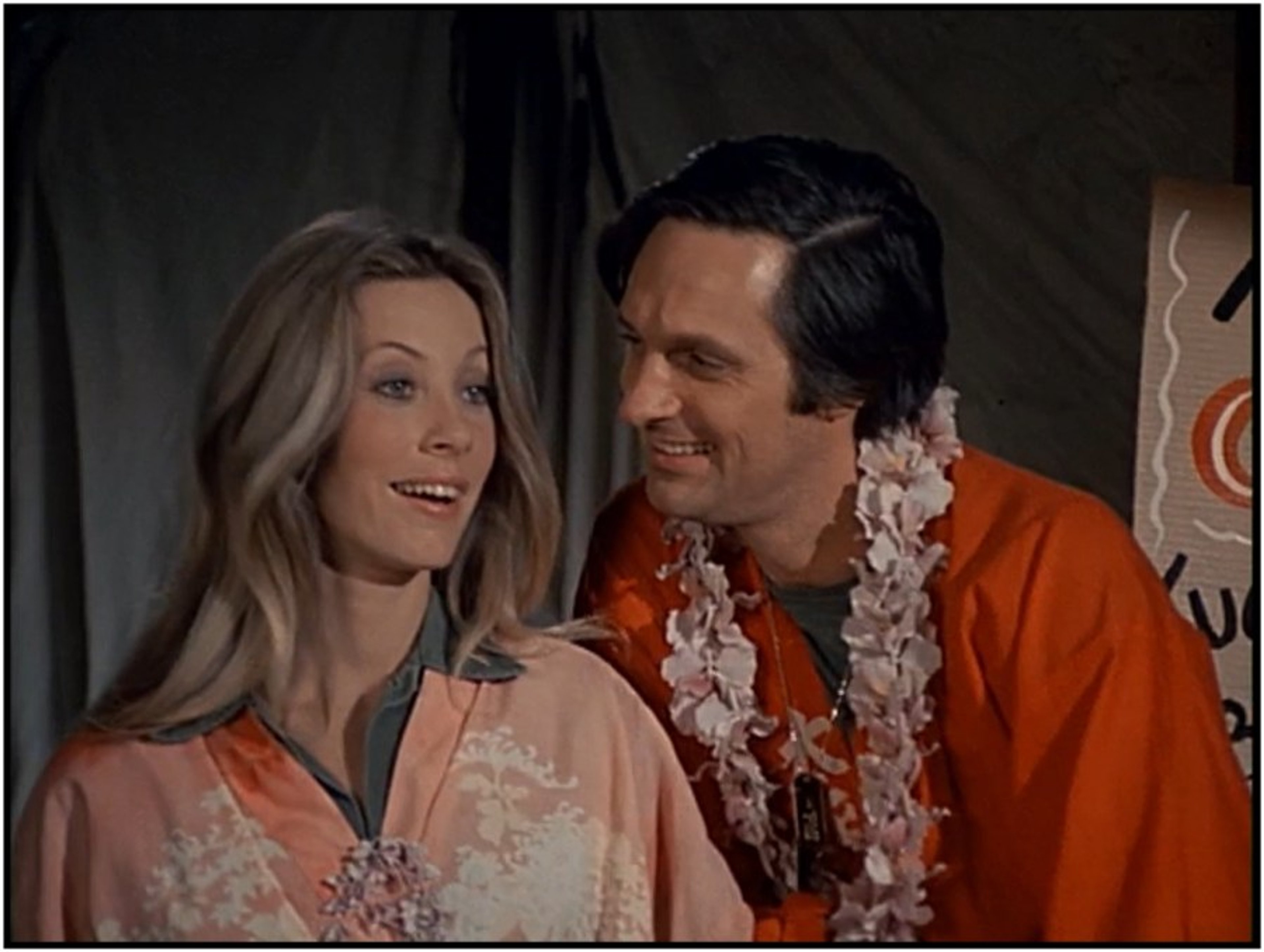 A blonde woman and a man in military uniforms standing together in a MASH unit setting