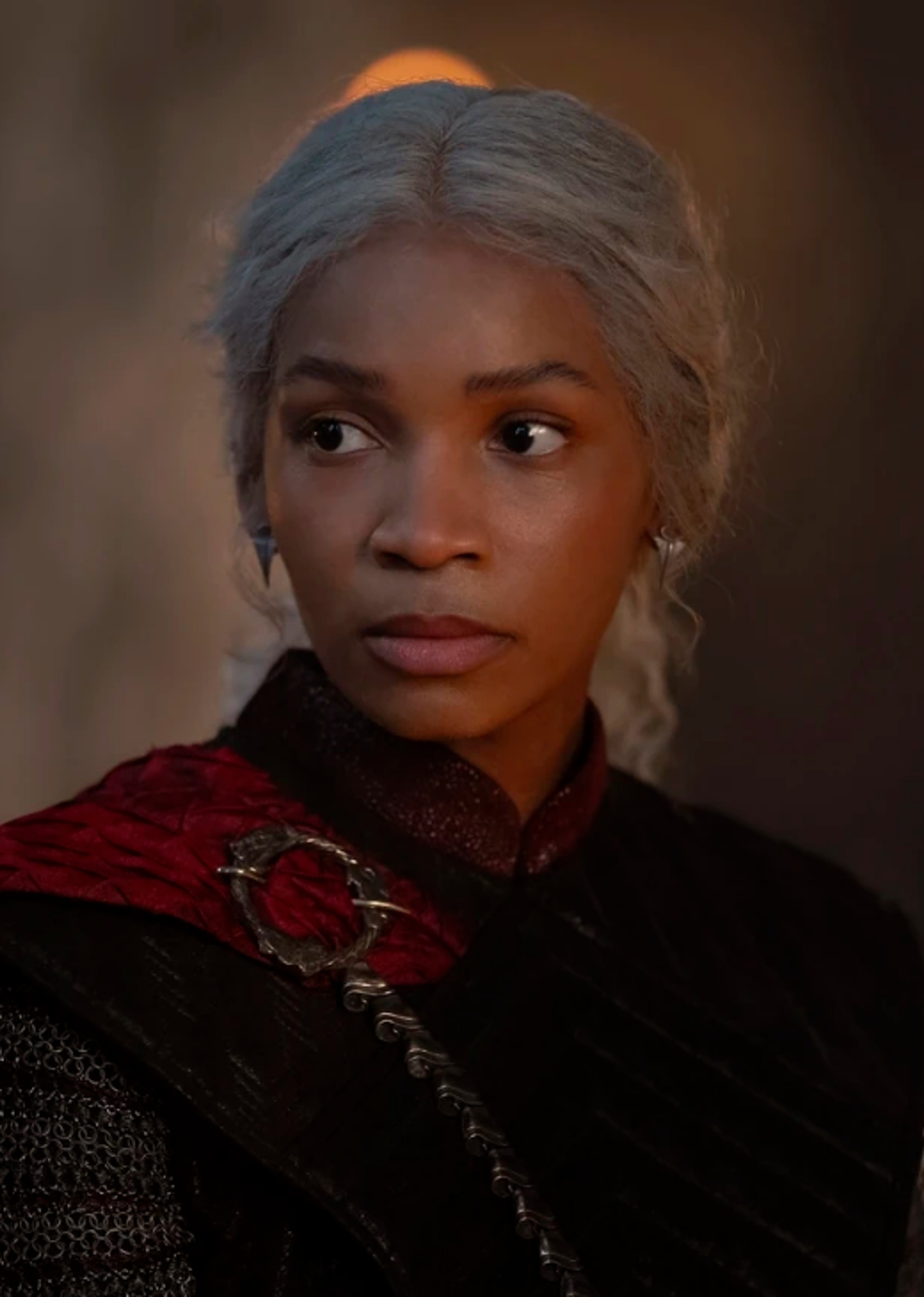 A woman with silver-white hair and a serious expression, wearing a dark red and black outfit with fur trim.