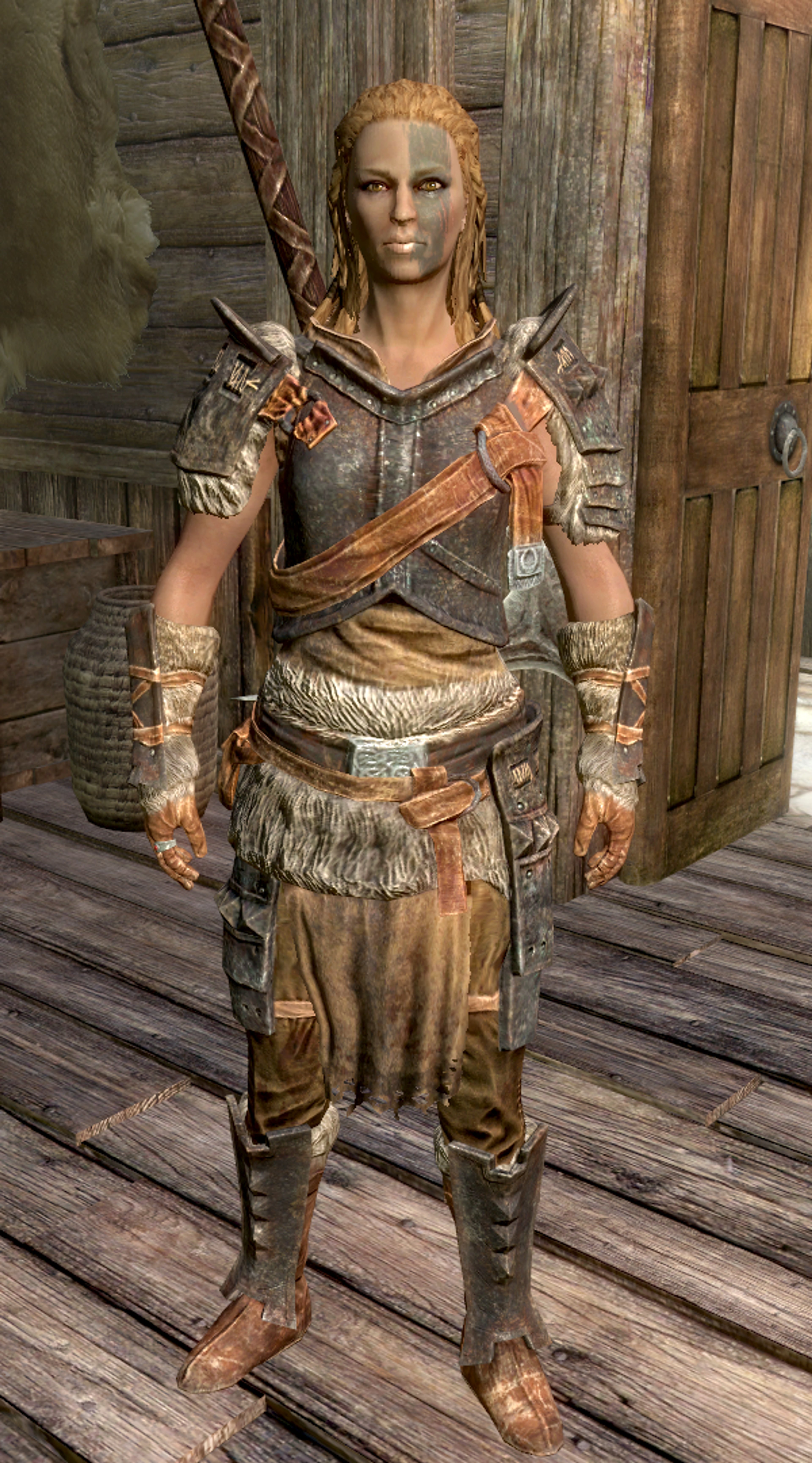 A female Nord warrior character with a muscular, weathered appearance, wearing heavy armor with fur accents and standing in a wooden structure.