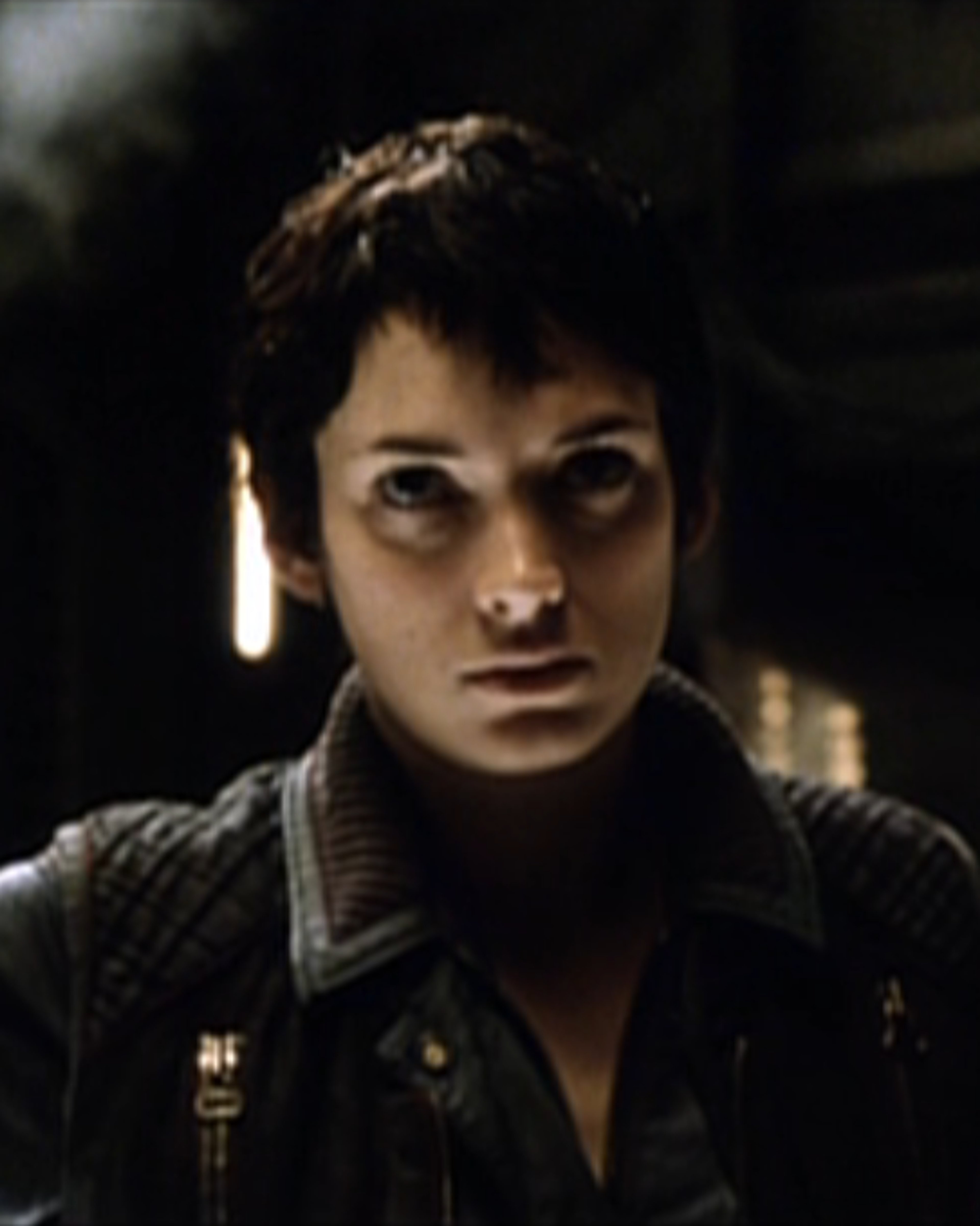 A close-up portrait of a young woman with dark hair and an intense, serious expression.