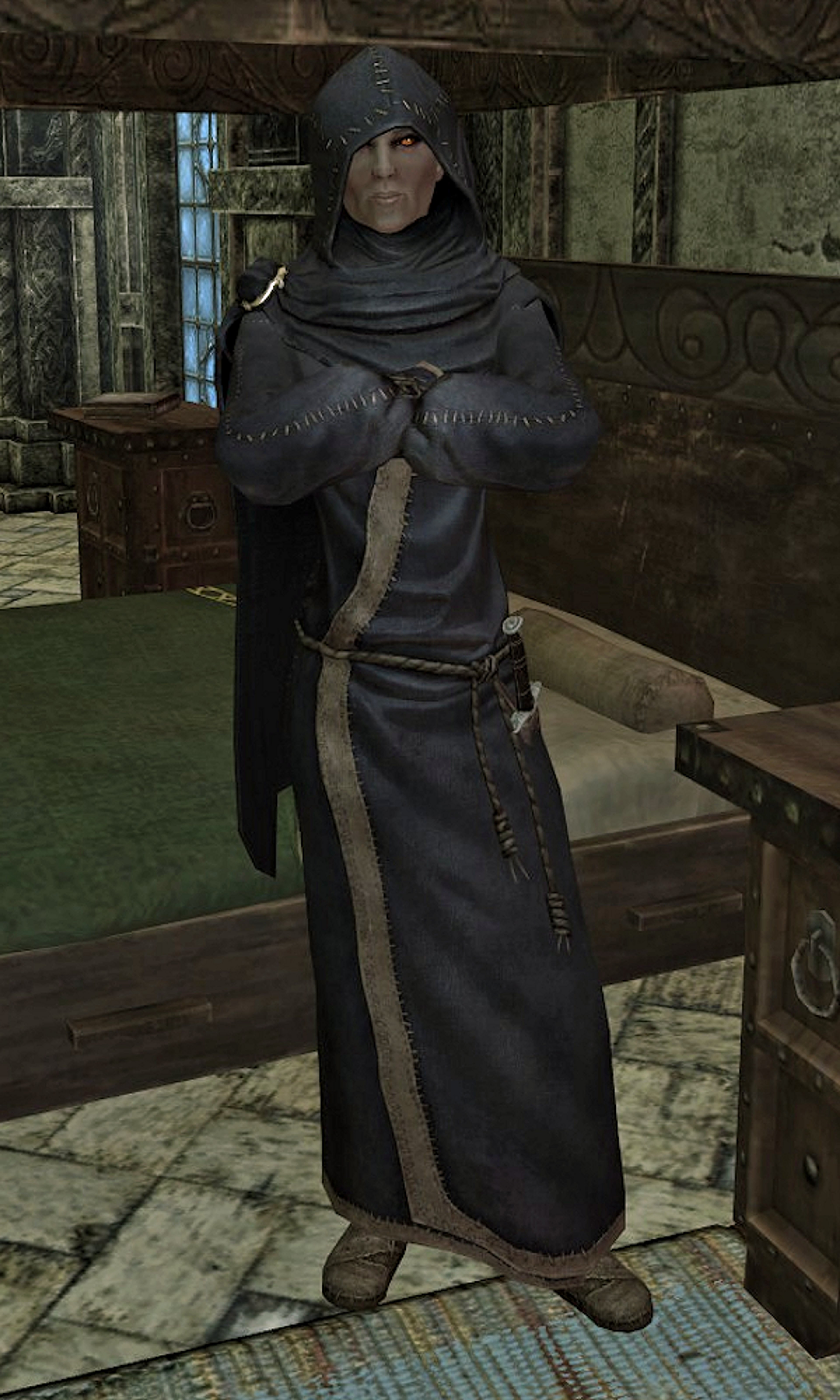 A Breton woman in a dark hooded robe standing in a dimly lit interior setting