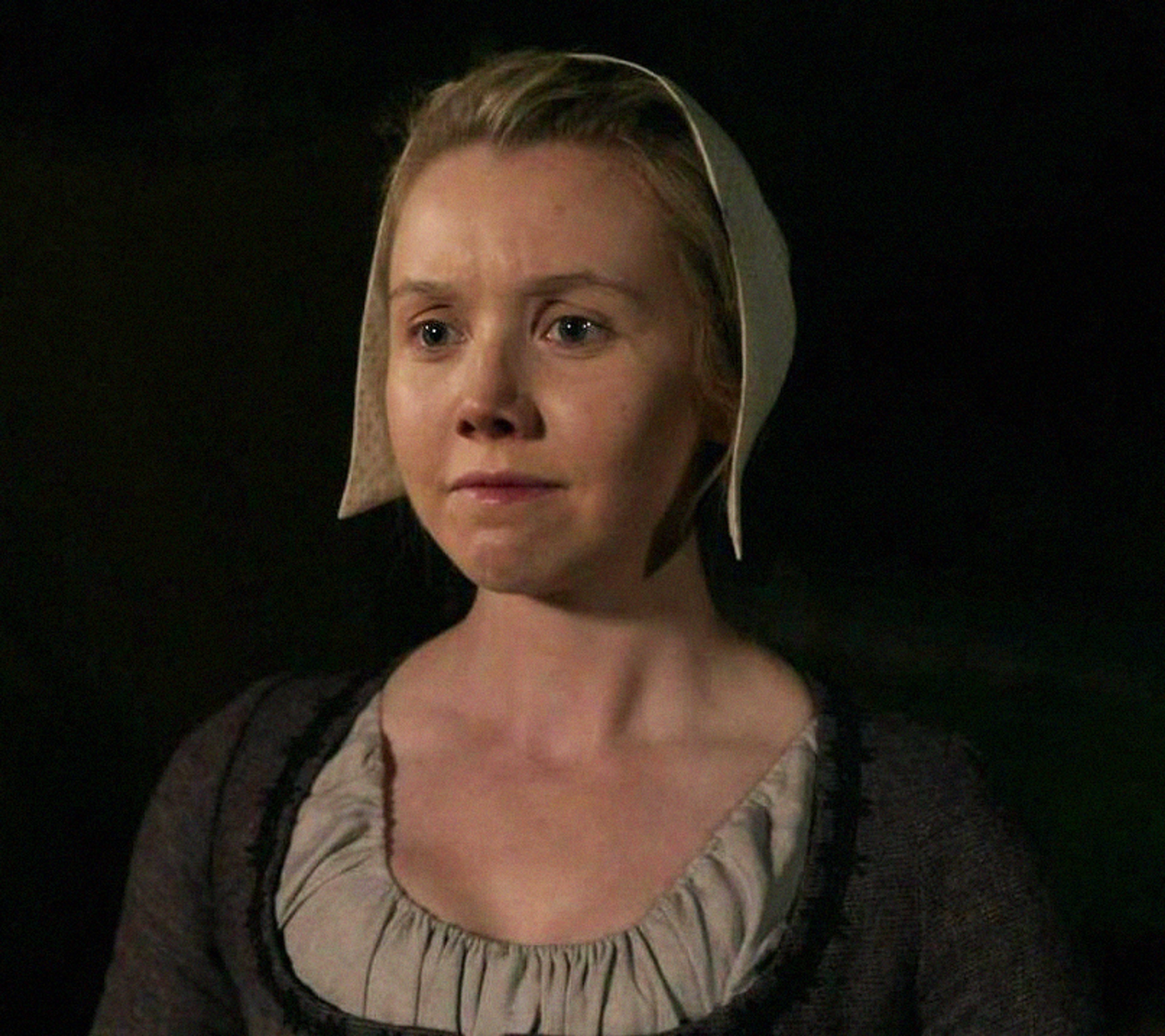 A portrait of a serious-looking blonde woman in a simple dress