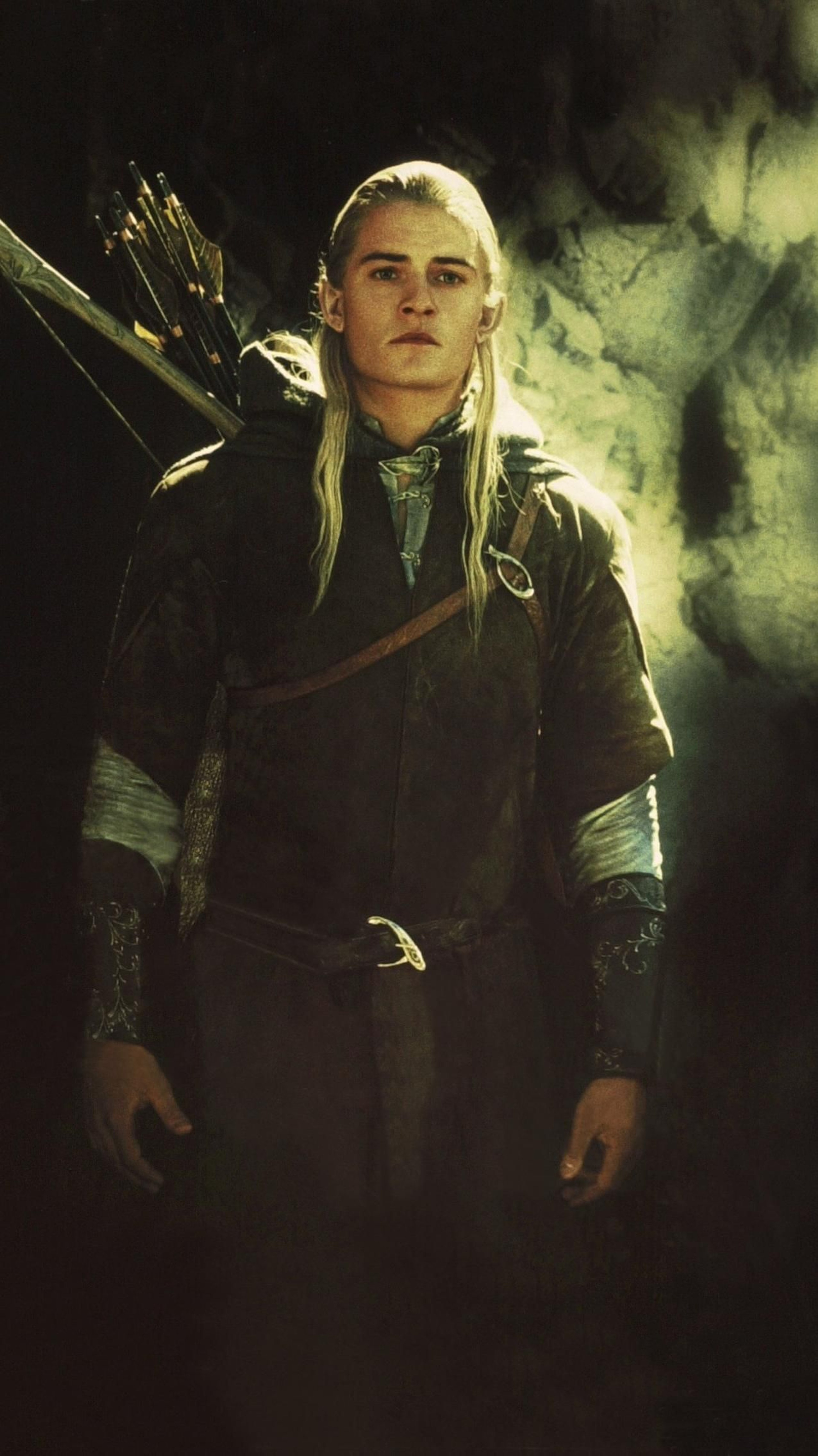 A male Elven character with long blonde hair, wearing a dark green cloak and holding a bow in a forest setting.