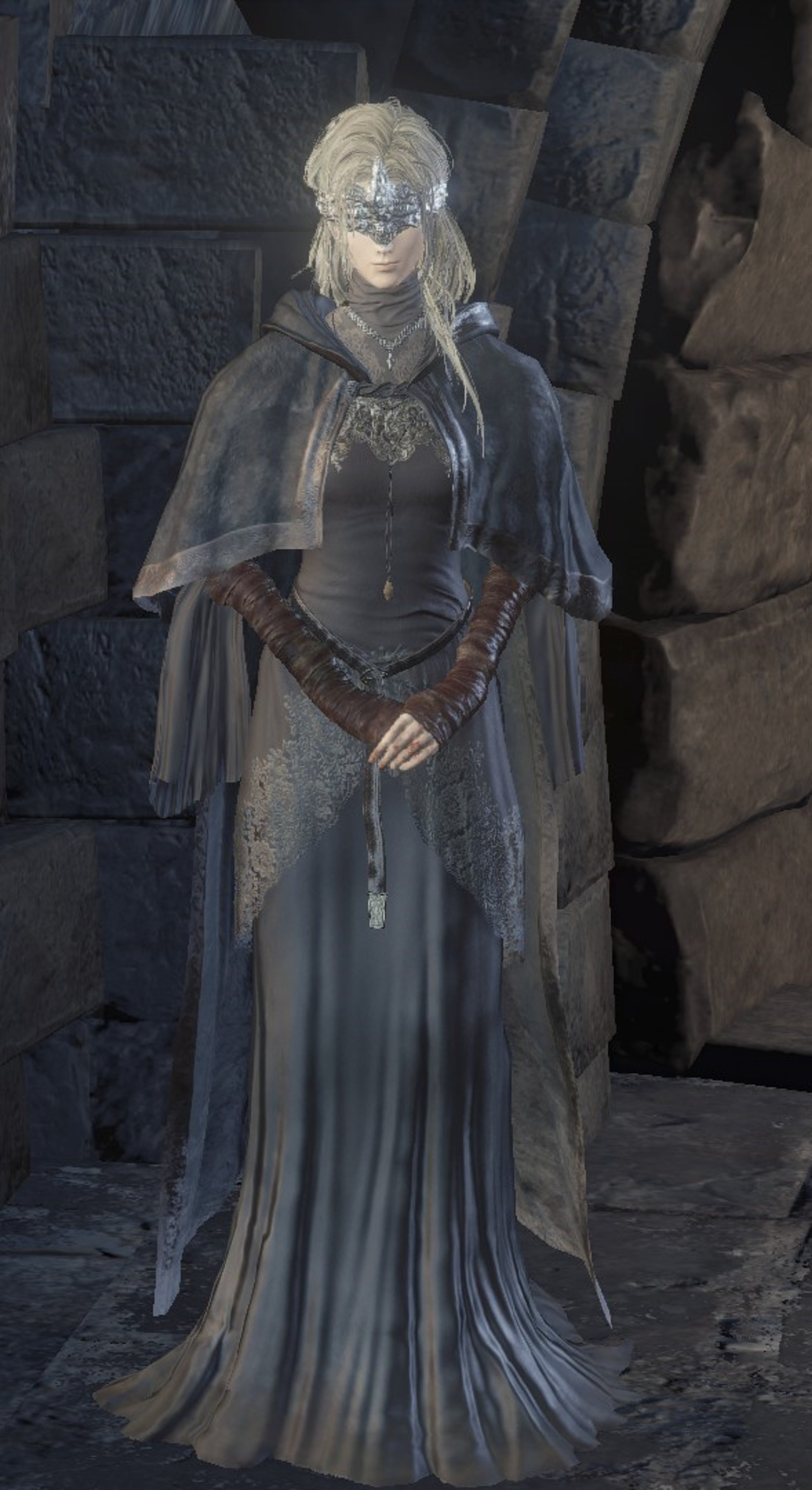 A mysterious, blind maiden in a long, gray dress and hooded cloak, standing in a dark, rocky environment.