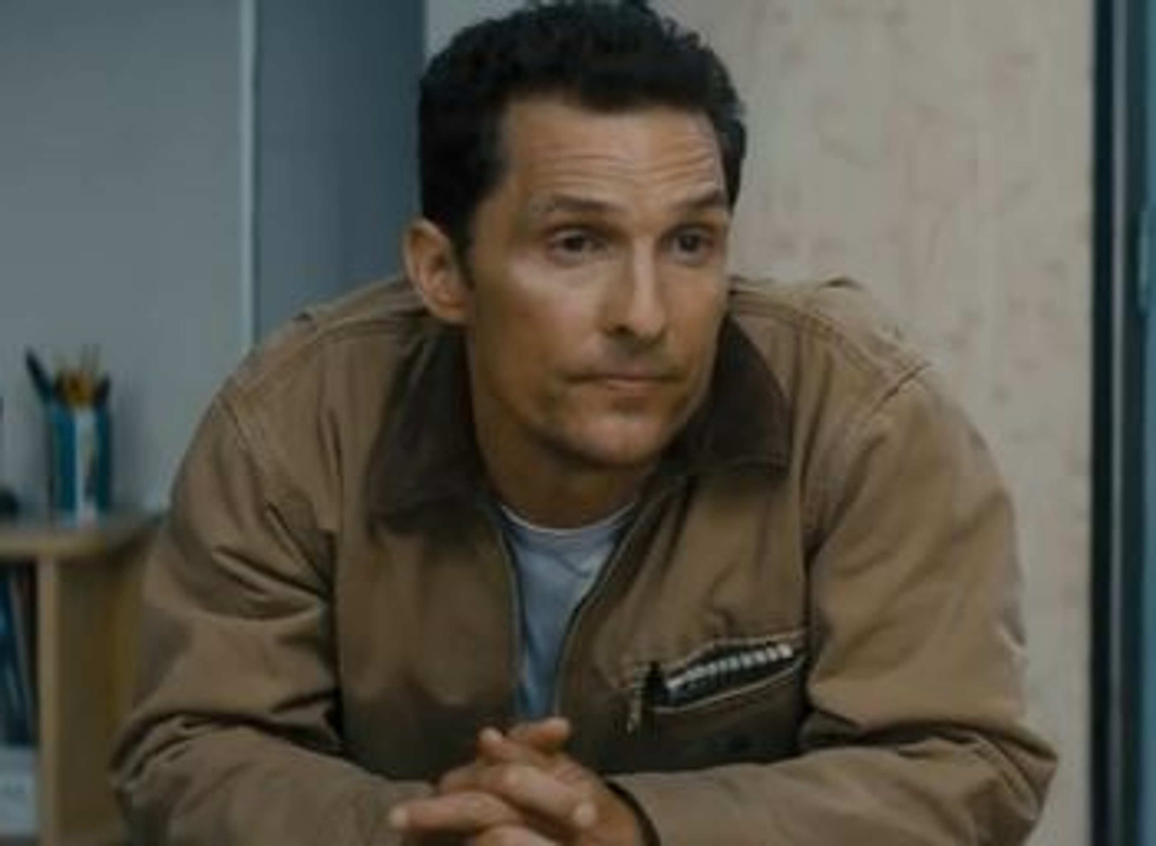 A middle-aged man with short dark hair and a beard, wearing a tan jacket, with a serious expression on his face.