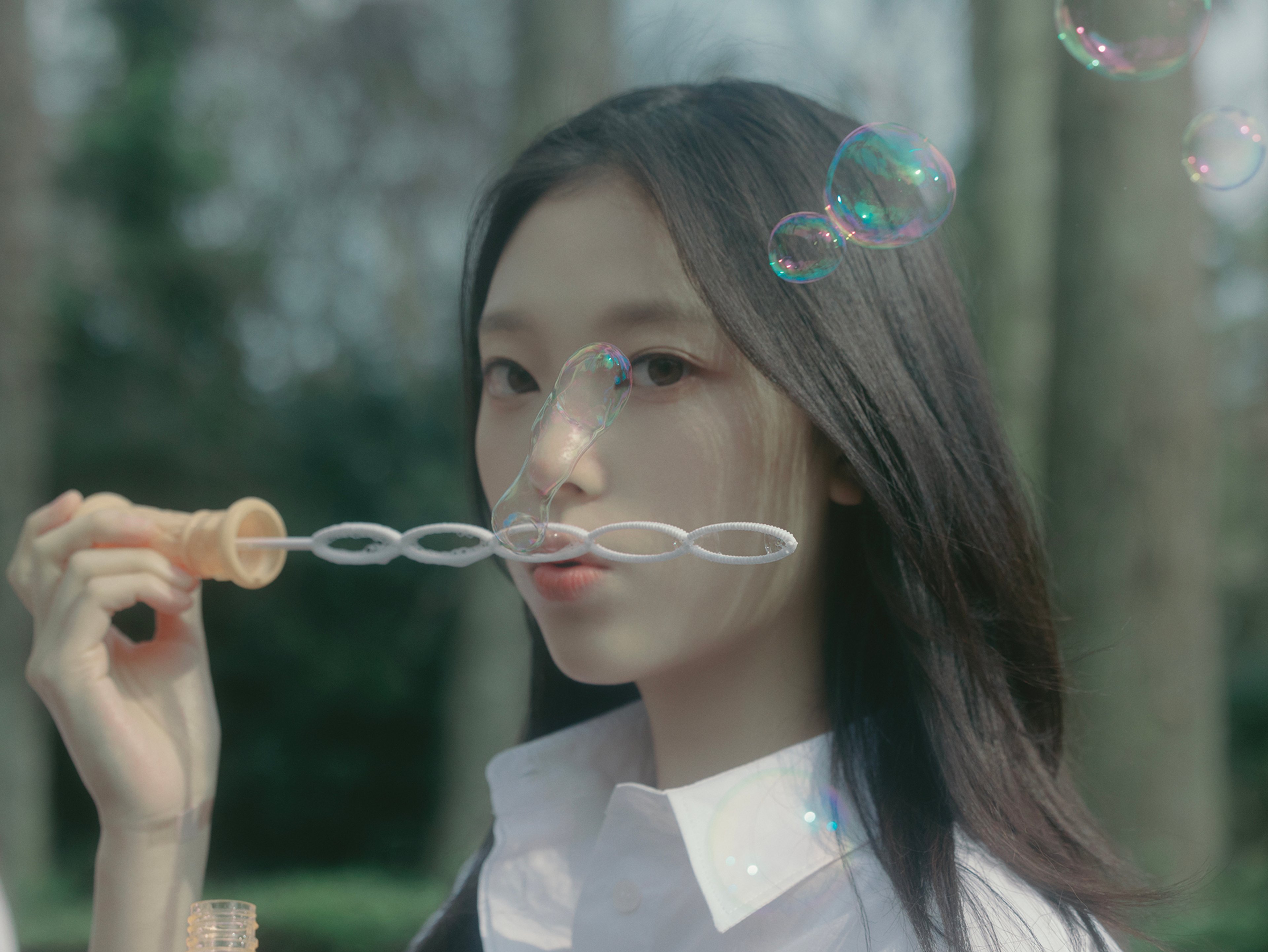 A young woman with long dark hair blowing bubbles in a natural outdoor setting.