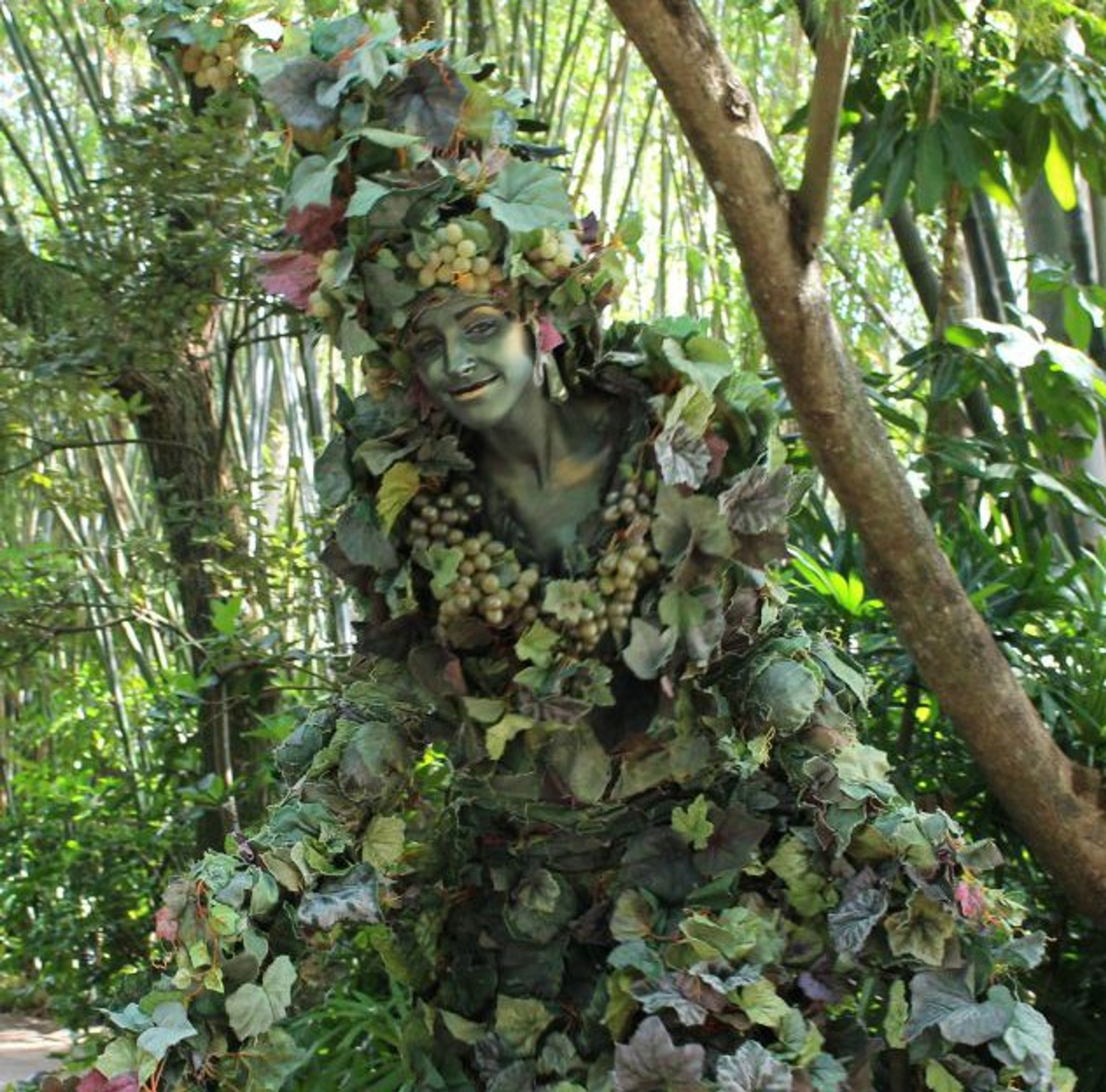 A figure covered in vines, leaves, and flowers, blending into a lush, green environment.
